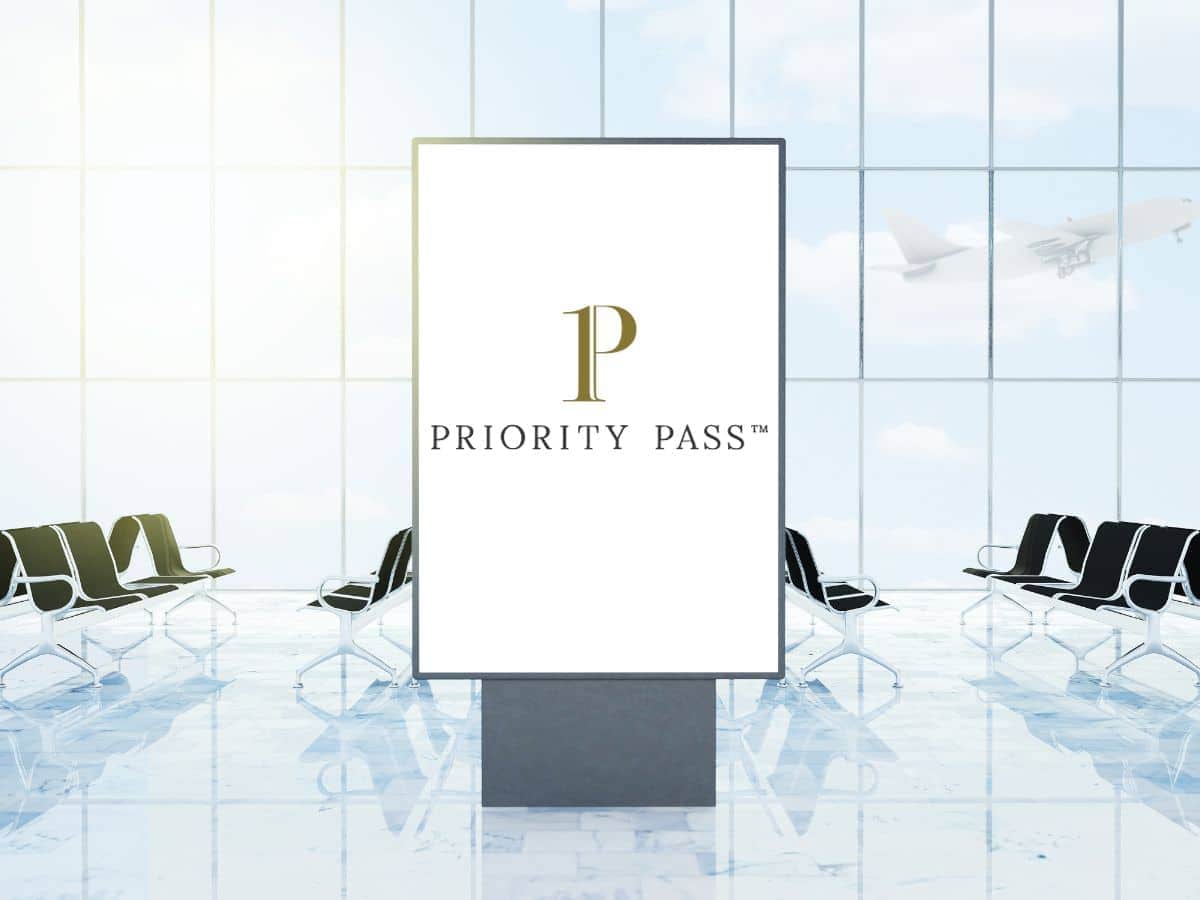An illuminated Priority Pass™ advertising stand in a modern airport lounge, with empty seating and a large window revealing a plane taking off in the background, posing the question: is Priority Pass worth it for serene travel experiences?