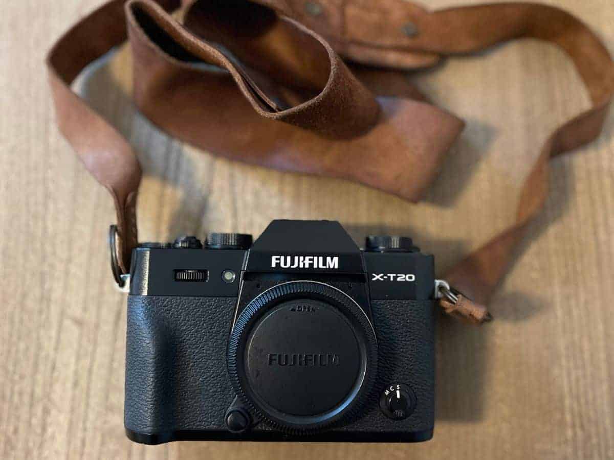 A Fujifilm X-T20 camera with a brown leather strap, an optimal choice for the best camera for solo travel, laid on a wooden surface.