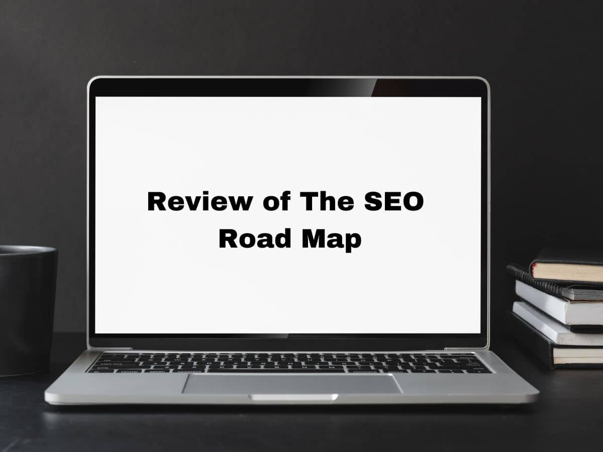 Open laptop with the text 'Review of The SEO Road Map' on screen, placed on a dark desk with books and a mug beside it