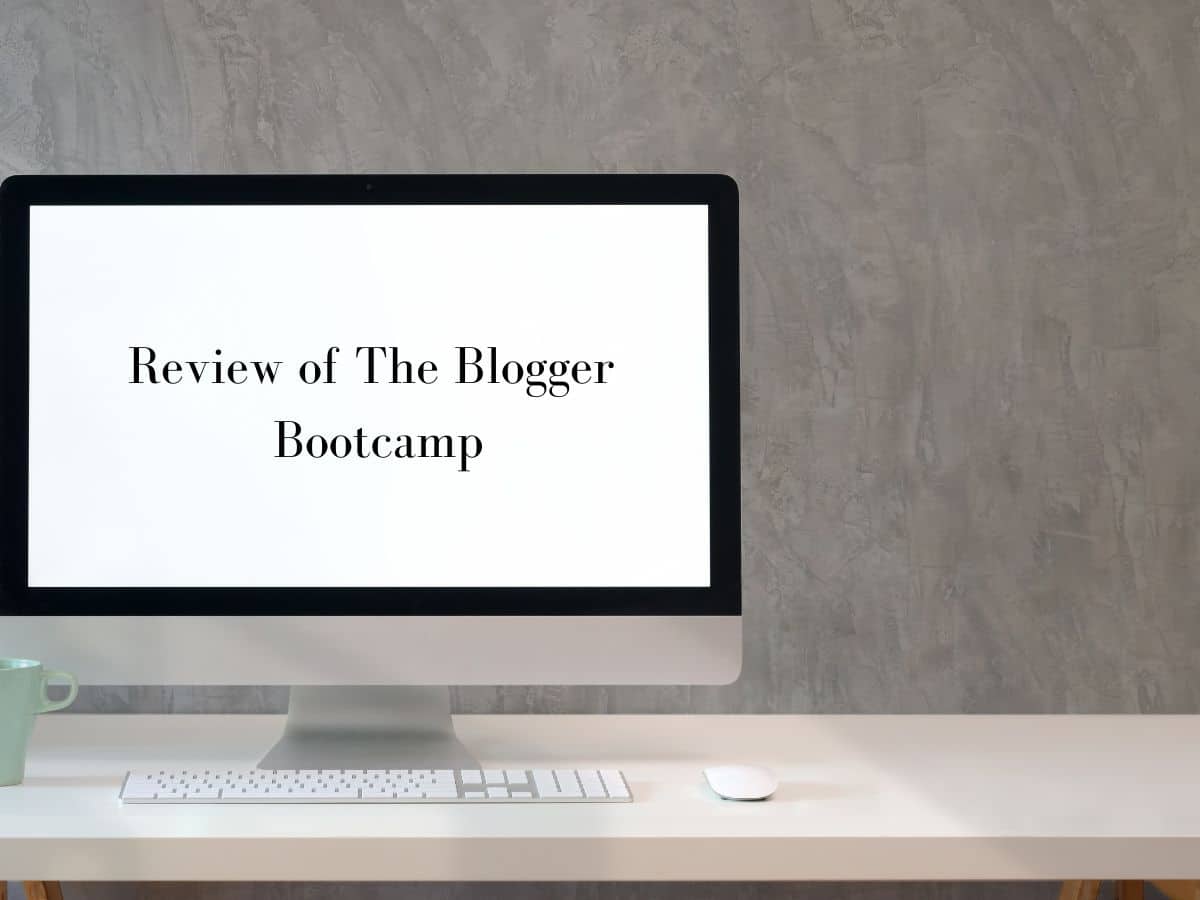 Computer monitor on a white desk displaying 'Review of The Blogger Bootcamp' with a gray wall in the background.