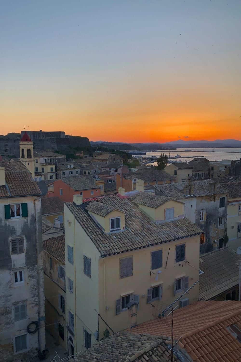 The bright orange sunset in Corfu, Geece with the colorful houses in the background.