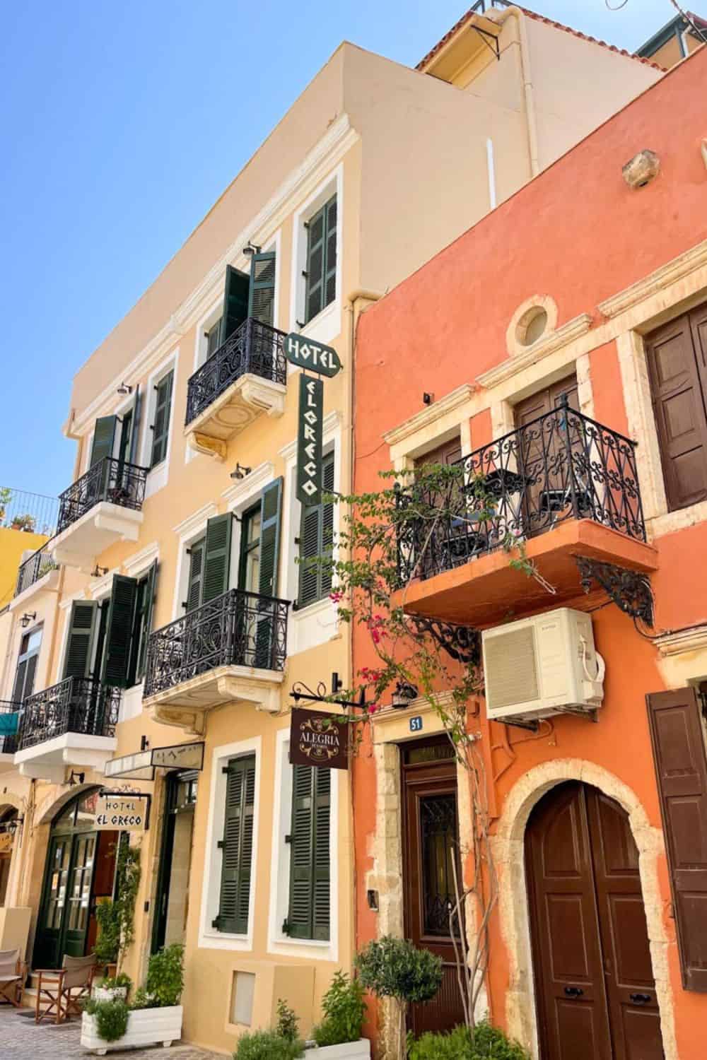 Colorful facades of Chania's old town buildings, with a view of the Hotel El Greco and Alegria signages, showcasing Greek architecture