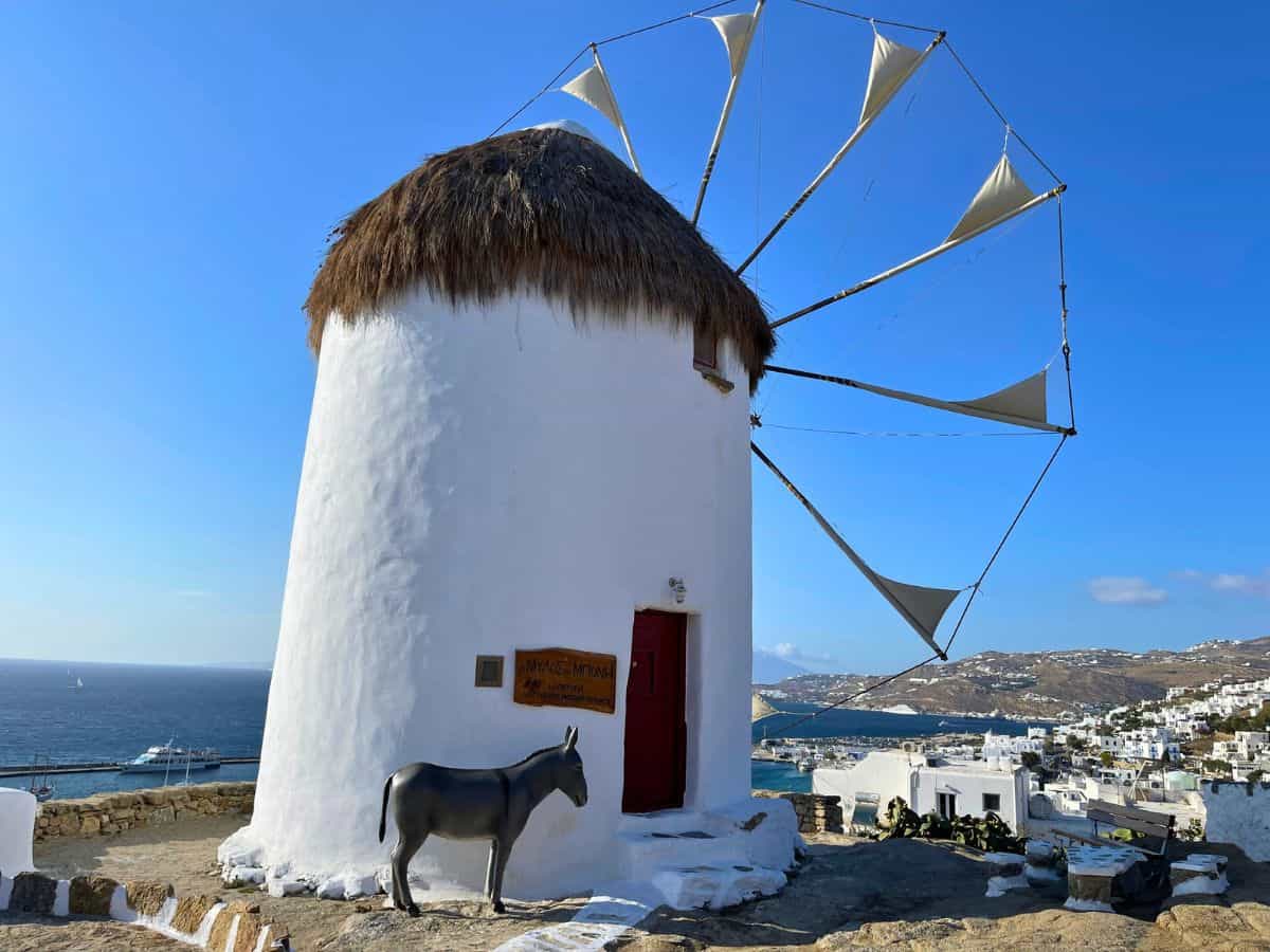 An iconic Greek Windmill with the sea and small town in the distance. 