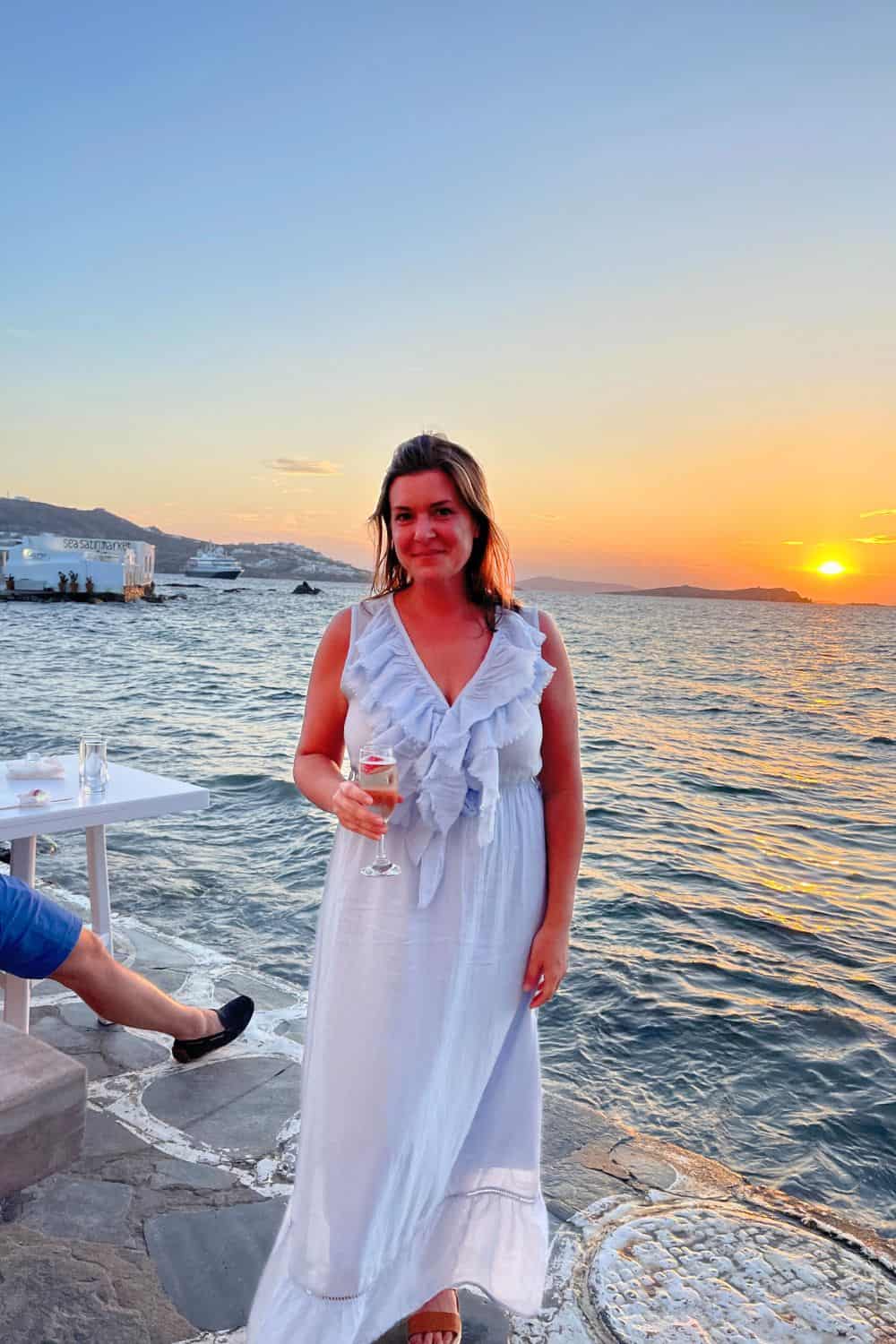 A woman in a blue dress standing at the sunset in Mykonos. 