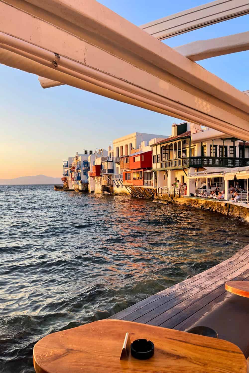 A picture of a sunset in Mykonos with the ocean up against the colorful buildings and balconies. 