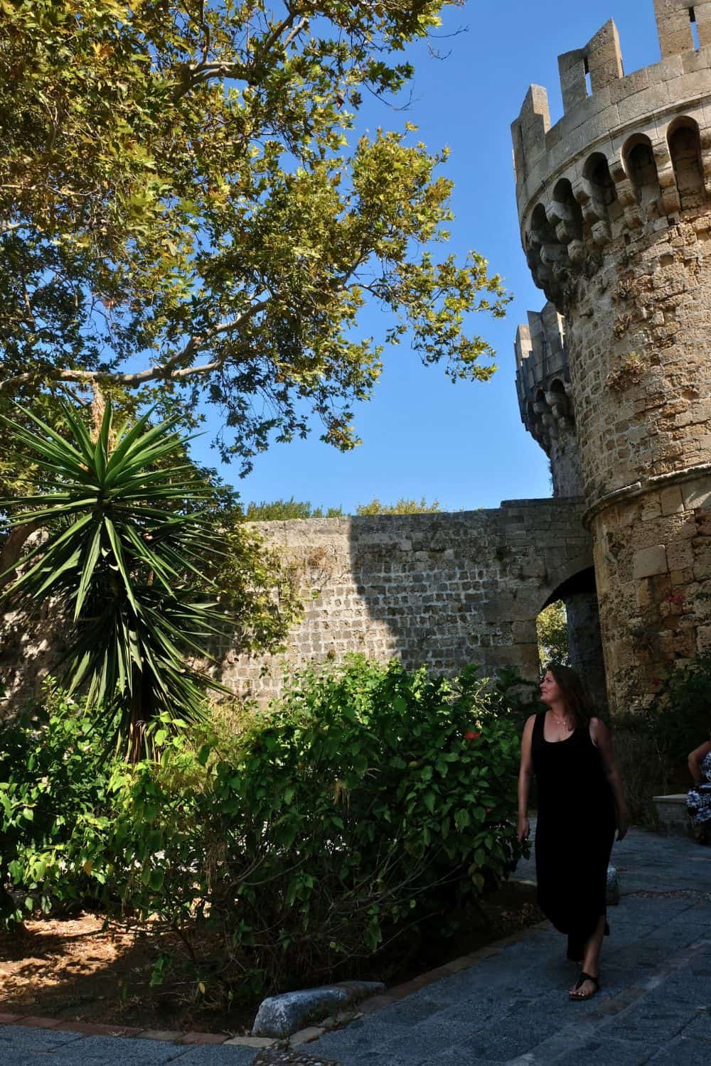 A woman walking along in Rhodes with the old city walls in the backgrond.