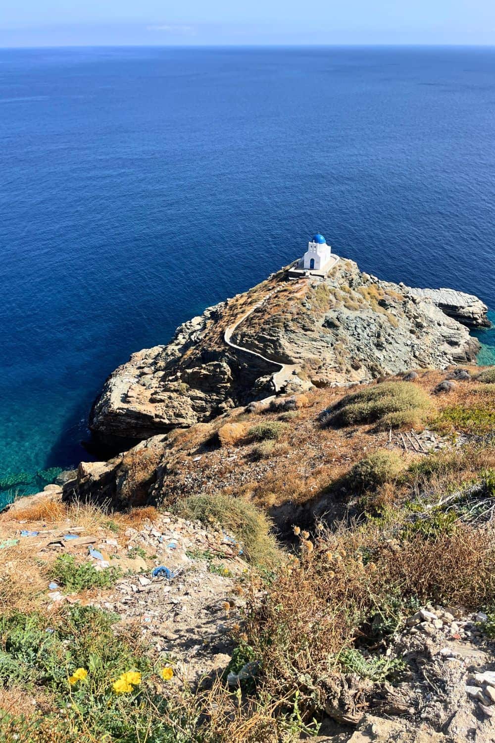 A traditional Greek chapel with a blue dome stands alone on a rocky outcrop overlooking the deep blue sea in Sifnos, Greece
