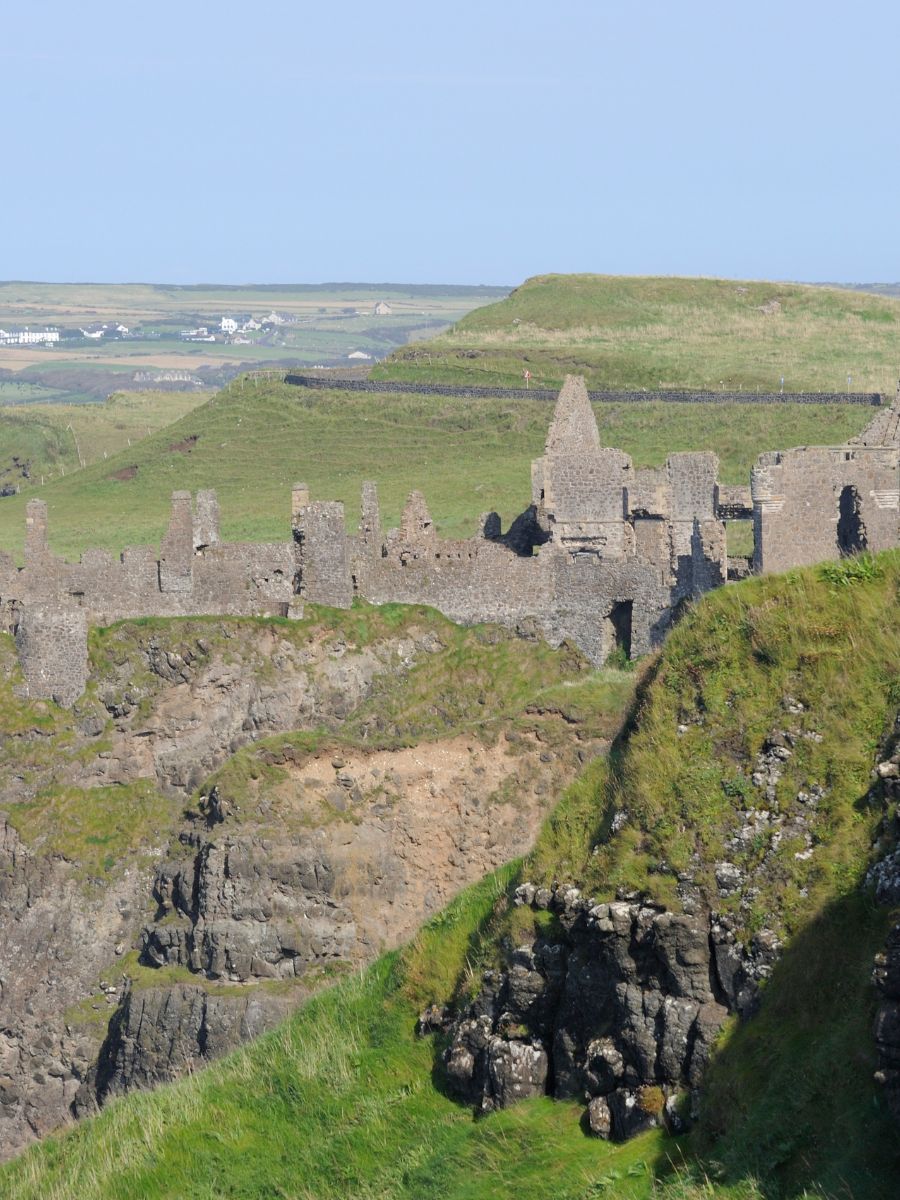 A panoramic view of Dunluce Castle ruins extending into the distance, with the contrasting green fields and the rugged cliff faces emphasizing its dramatic location.