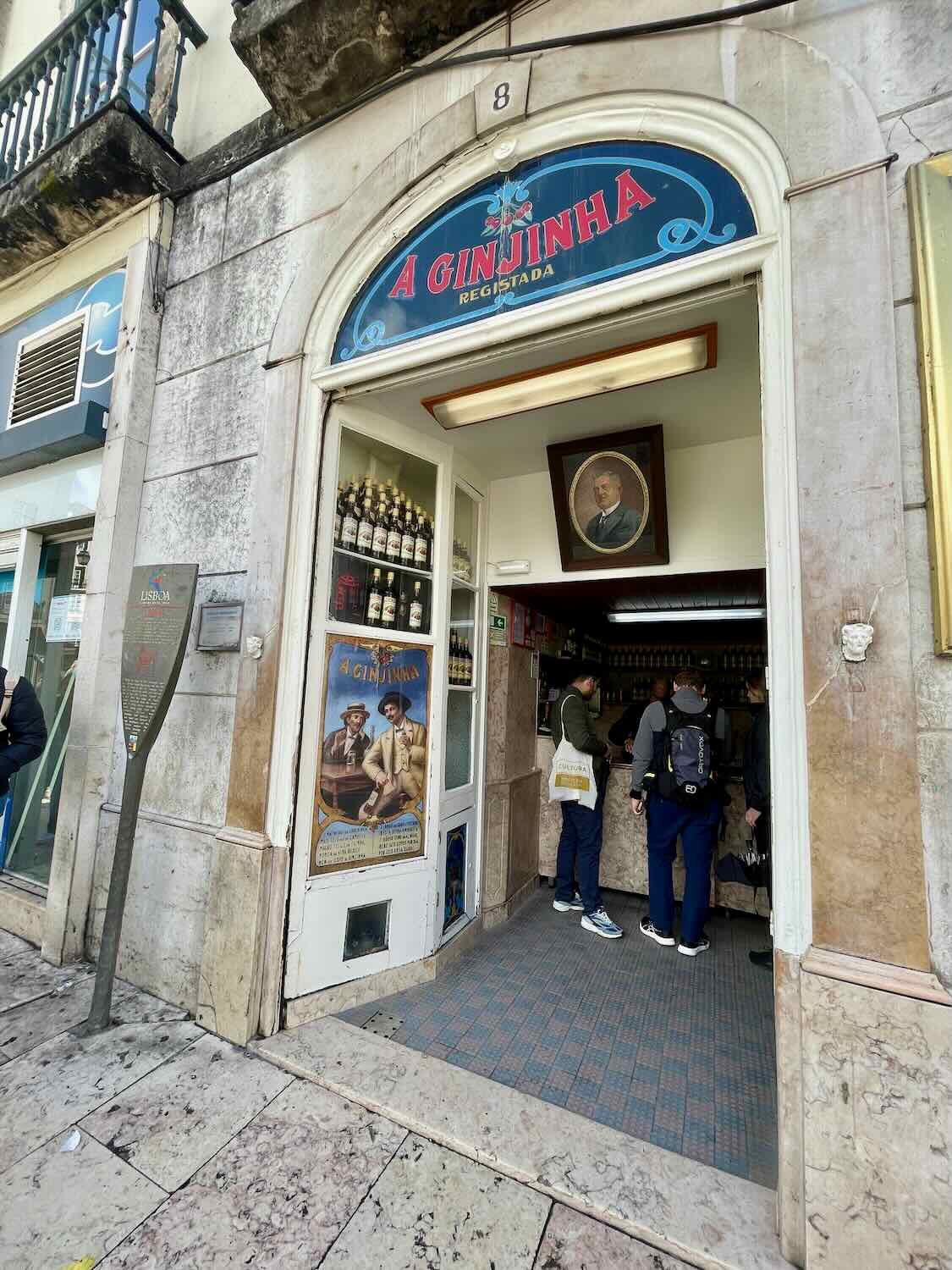 Patrons at the entrance of 'A Ginjinha', a traditional Lisbon establishment famous for its sour cherry liqueur, highlighting a unique local experience.