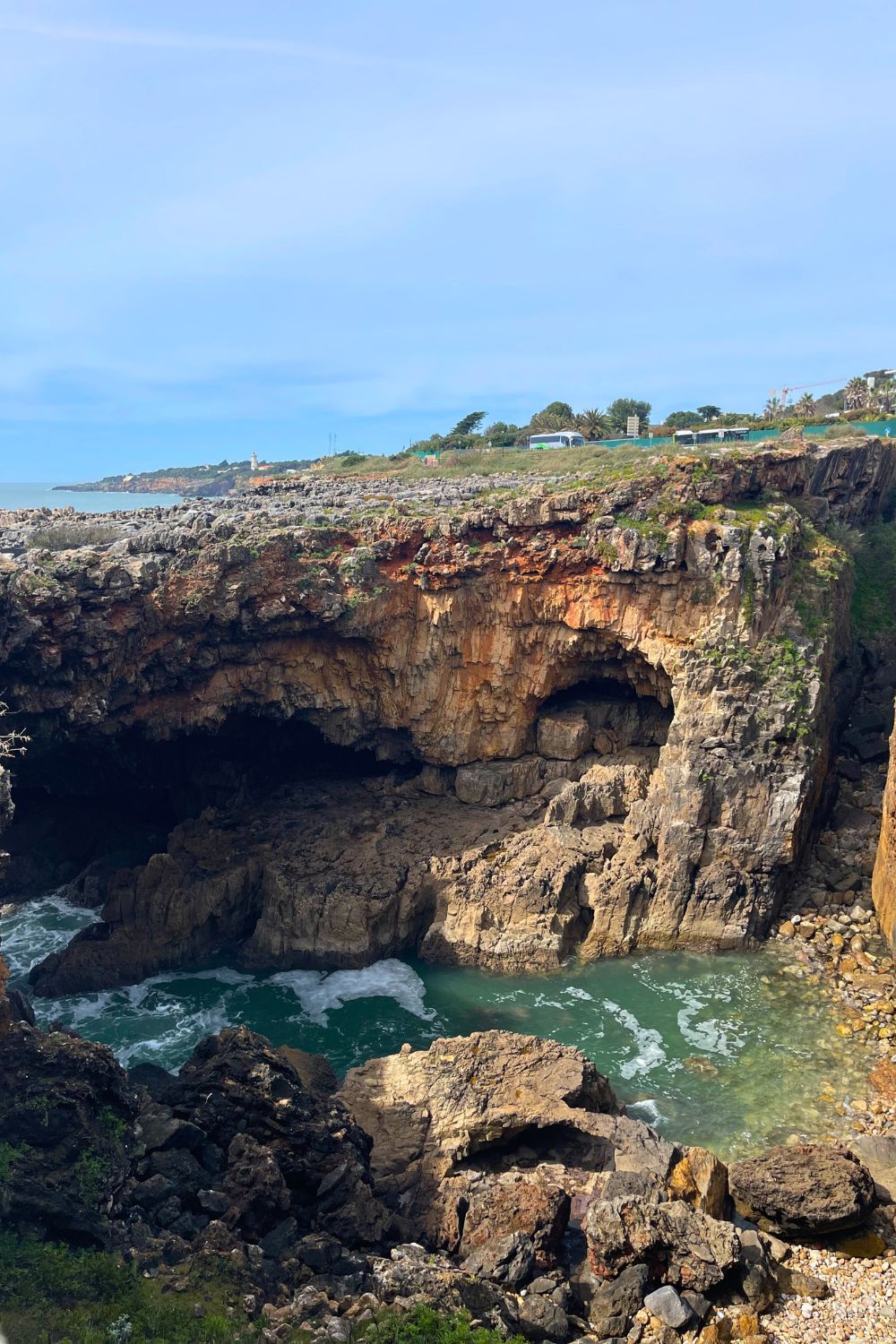 A breathtaking view of the natural rock formation known as Hell's Mouth (Boca do Inferno) in Cascais, with a rugged cliff face overlooking a serene sea. The image captures the beauty of the cavernous area where the azure waters of the Atlantic Ocean surge with a tranquil force