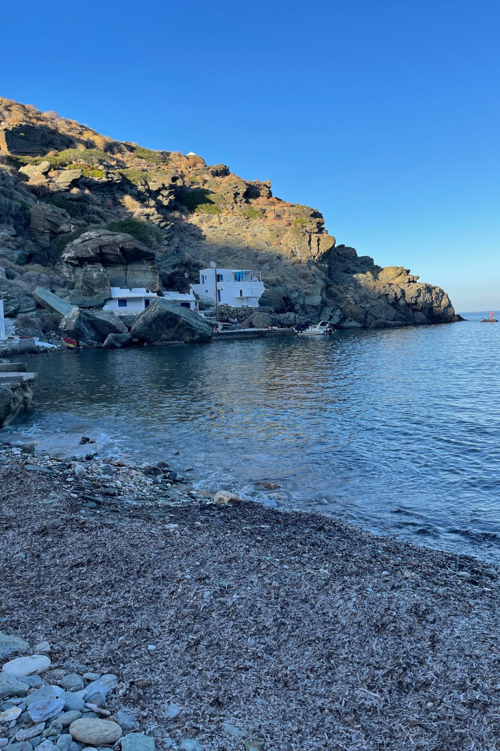 Secluded Kastro Beach in Sifnos framed by rugged cliffs and a white-washed building, reflecting the tranquility of the Aegean Sea
