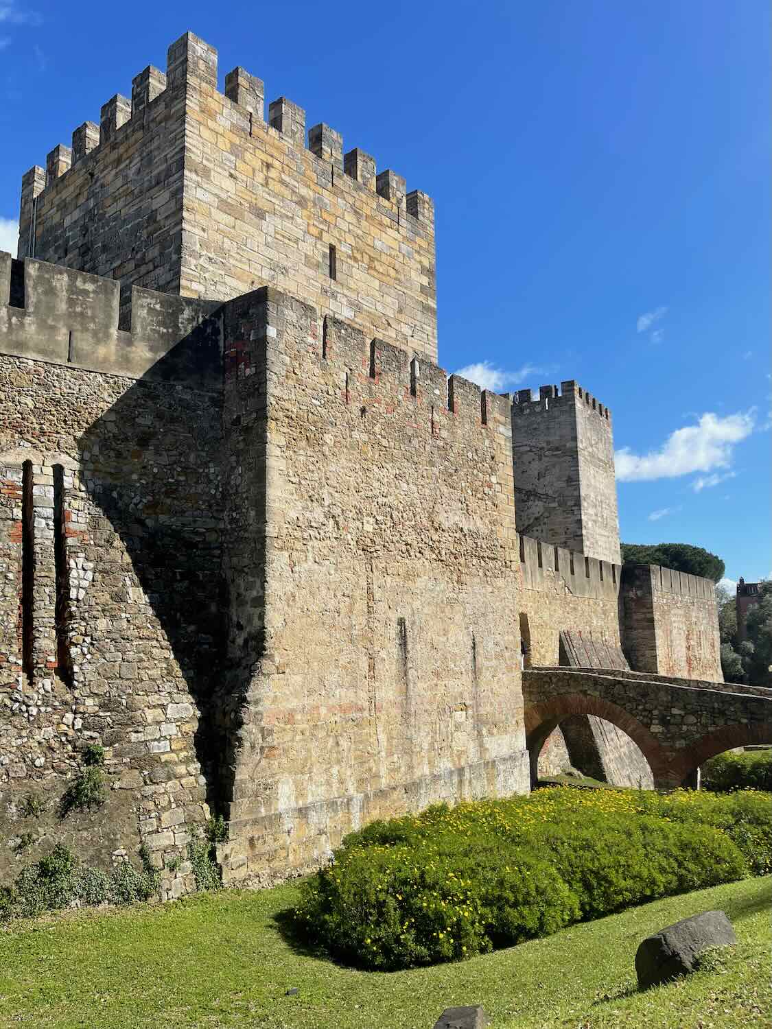The imposing walls and towers of São Jorge Castle under a bright blue sky, a testament to Lisbon's medieval history and a popular viewpoint for panoramic cityscapes