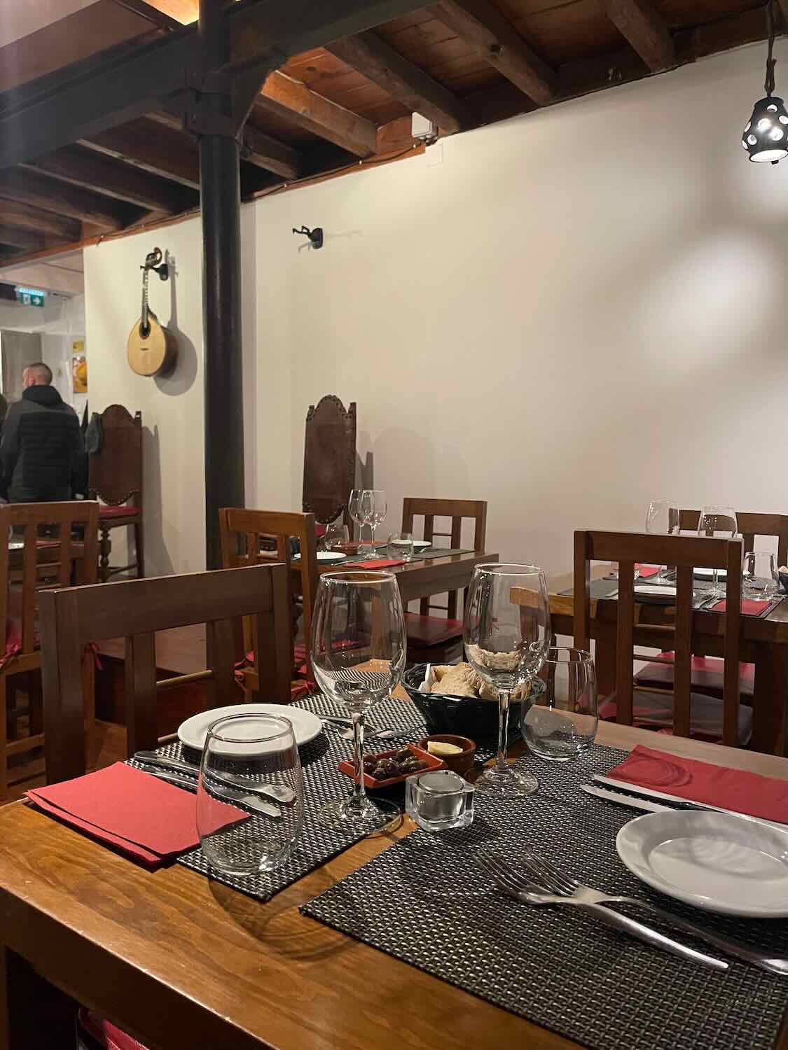A cozy Lisbon restaurant set for dinner with traditional Fado instruments displayed, inviting guests to a night of cultural immersion through music and cuisine.