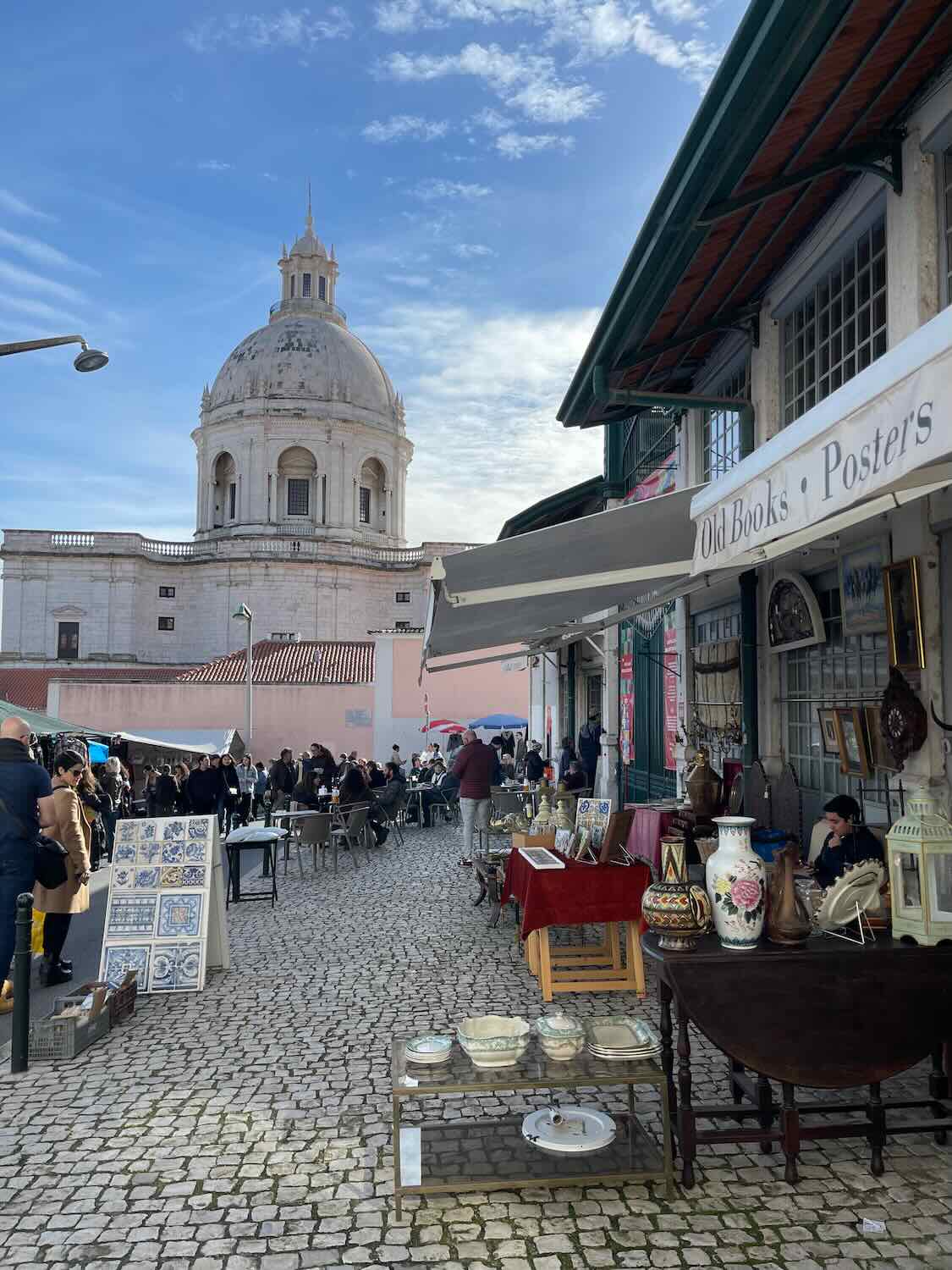 A lively Lisbon market near a historic building, where locals and tourists browse through antique items and vintage collectibles under the sun.