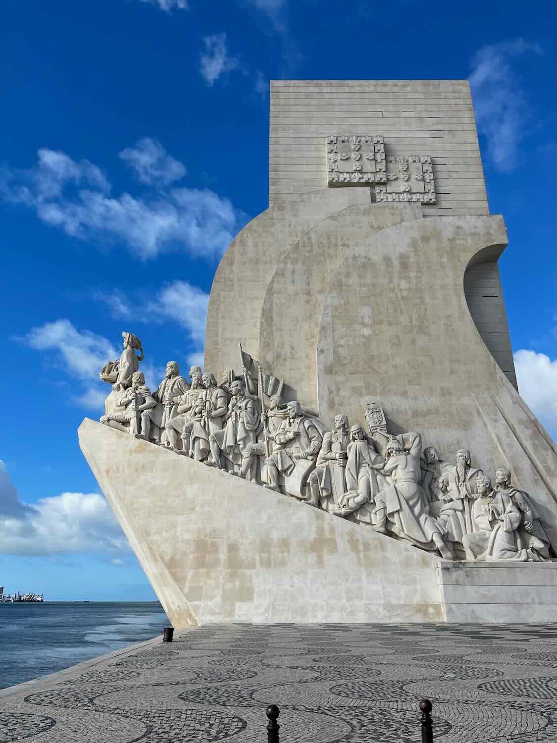 The iconic Padrão dos Descobrimentos monument in Lisbon, celebrating the Portuguese Age of Discovery, against a bright blue sky with sculpted figures of explorers.