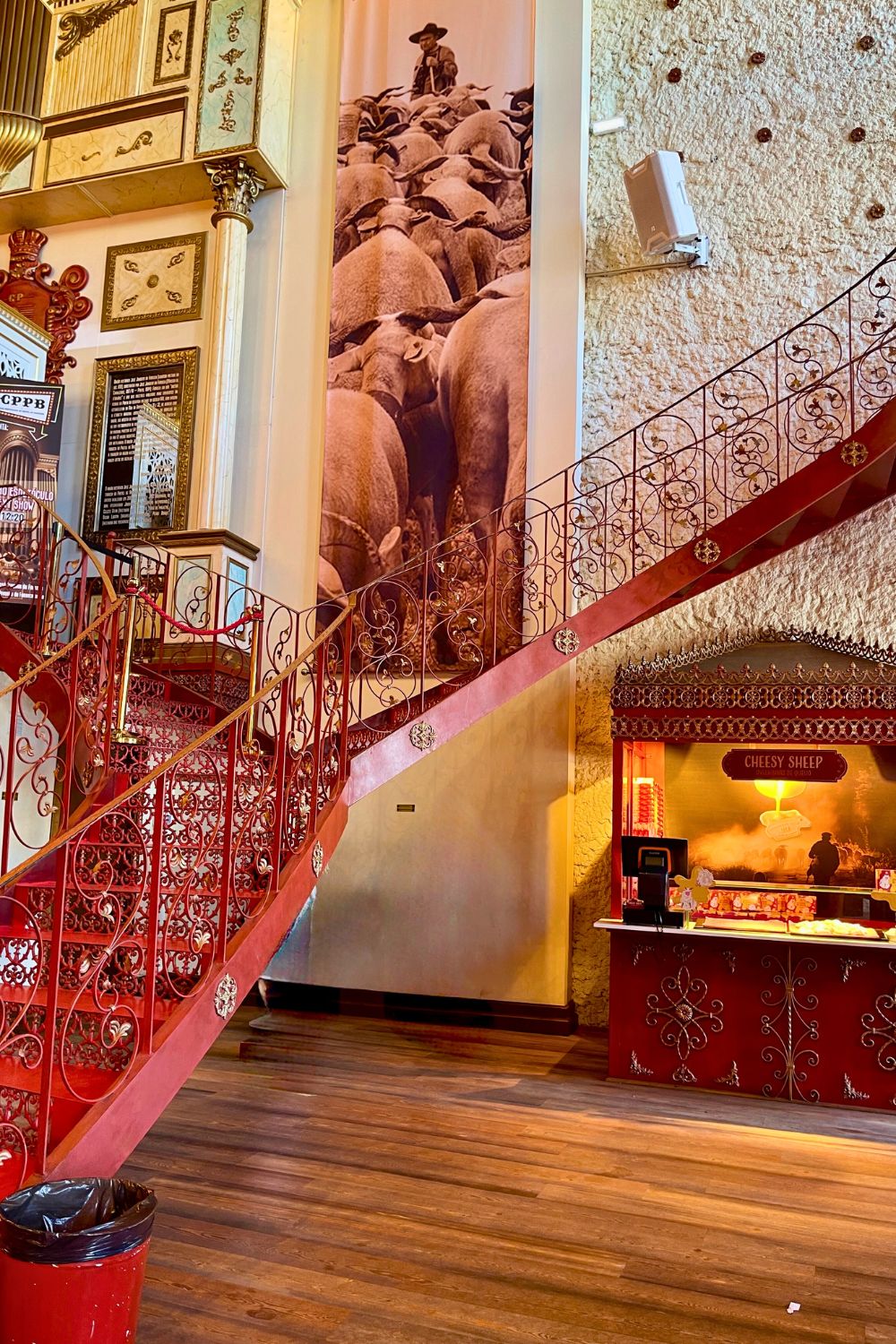 An ornate red staircase with decorative ironwork inside a vibrant and eclectic interior, featuring a large historic photograph and a 'Cheesy Sheep' food counter