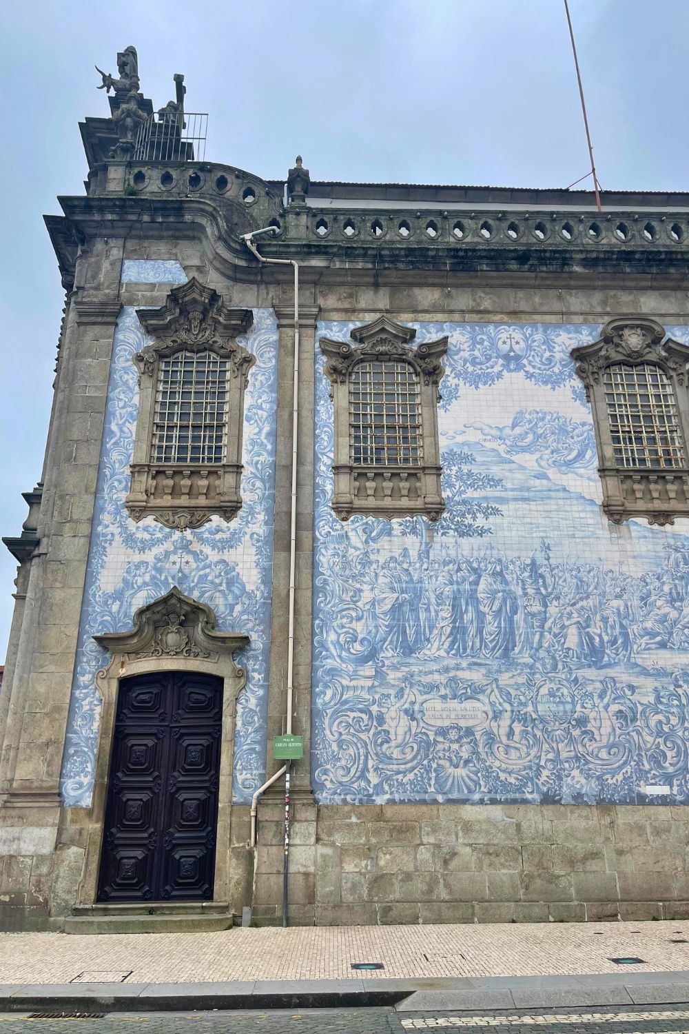 Facade of a church in Porto adorned with intricate azulejo tilework, showcasing scenes in various shades of blue under a cloudy sky.