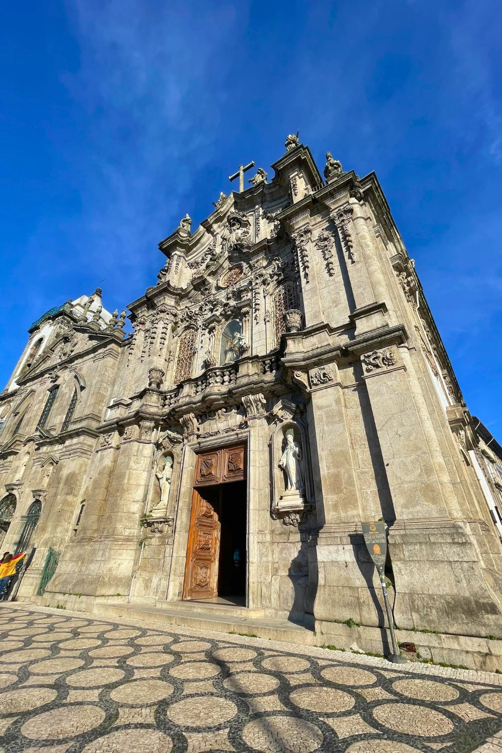 Exterior view of a grand baroque church in Porto under a clear blue sky, detailing its elaborate architecture and sculptural elements.