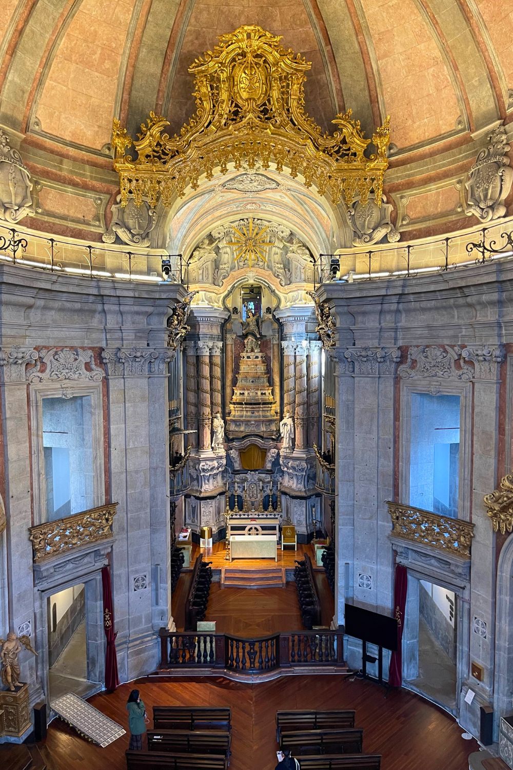 Interior view of a Porto church showing the elaborate gold leaf baroque altar, ornate woodwork, and grand arches, as seen from the upper-level balcony.