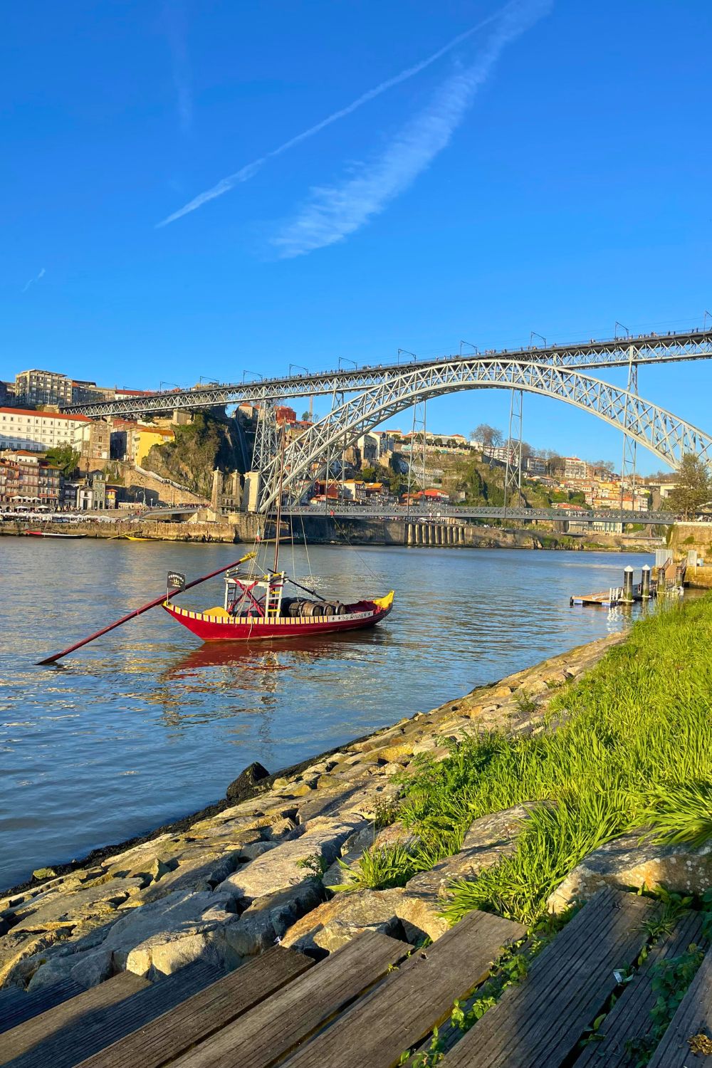 Traditional Rabelo boat moored on the calm waters of the Douro River with the iconic Dom Luís I Bridge arching overhead against a clear blue sky