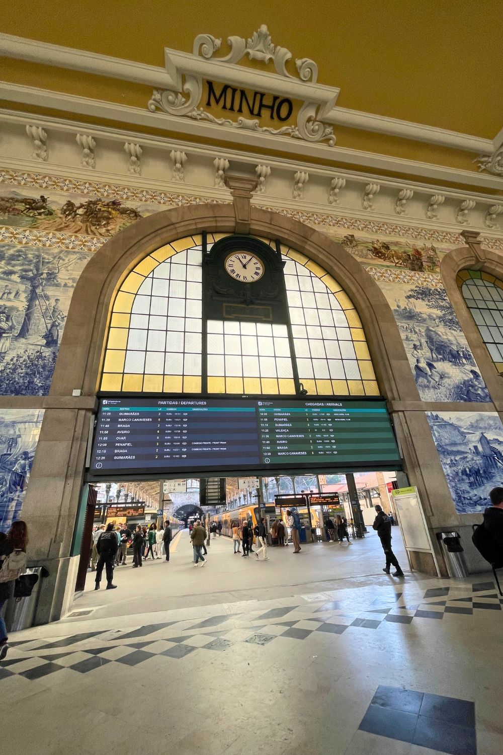 The grand interior of São Bento Railway Station in Porto, with its historic clock and azulejo tile panels depicting scenes of Portuguese history.