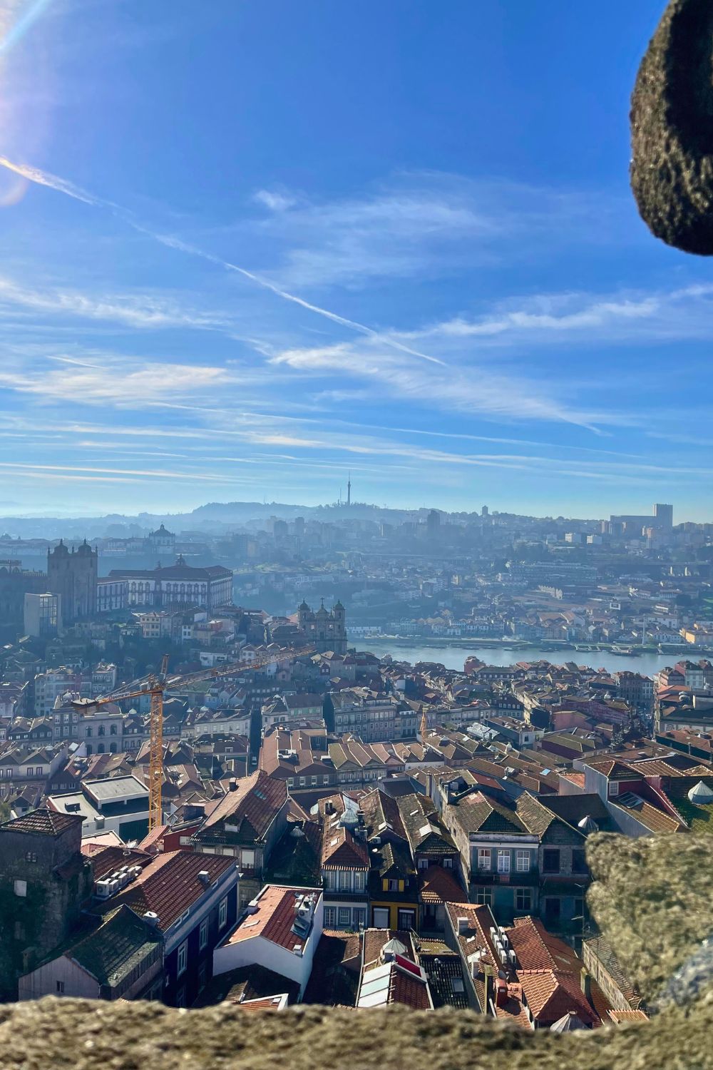 Scenic overlook of Porto's dense historic architecture and the Douro River, under a hazy blue sky with soft clouds, as seen from a high vantage point.