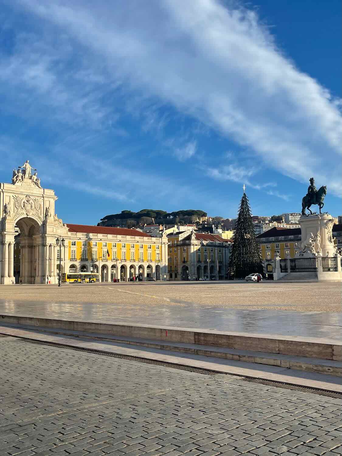 "Praça do Comércio

in Lisbon during winter, with a large Christmas tree set up in the square, the triumphal arch in the background, and a clear blue sky above.
