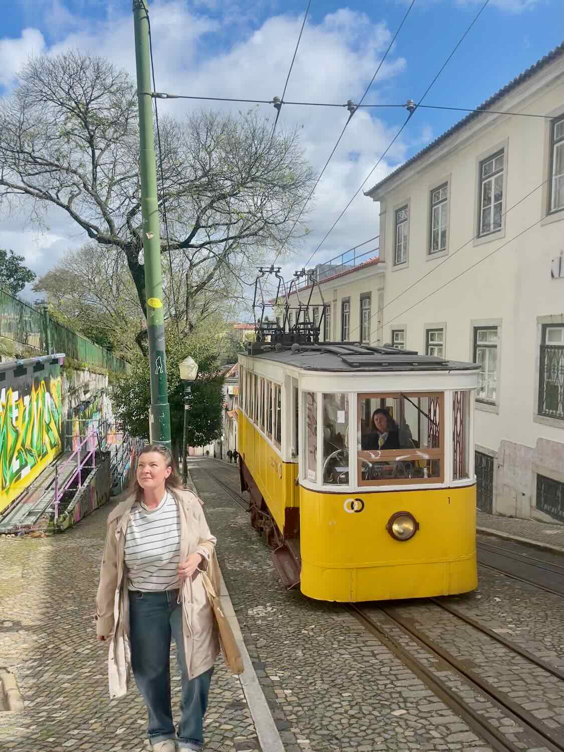 A solo traveler stands beside the iconic yellow Tram 28 in Lisbon, with traditional Portuguese buildings lining the street
