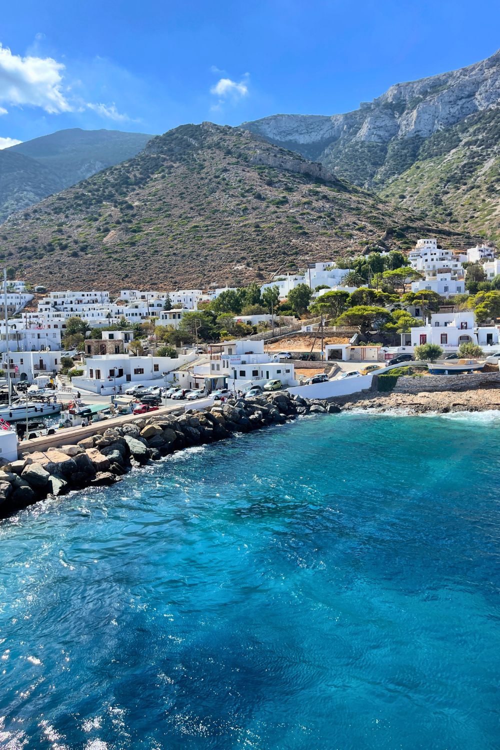 The picturesque harbor of Sifnos, featuring whitewashed buildings against a backdrop of rugged hills, with the crystal-clear waters of the Aegean Sea in the foreground.