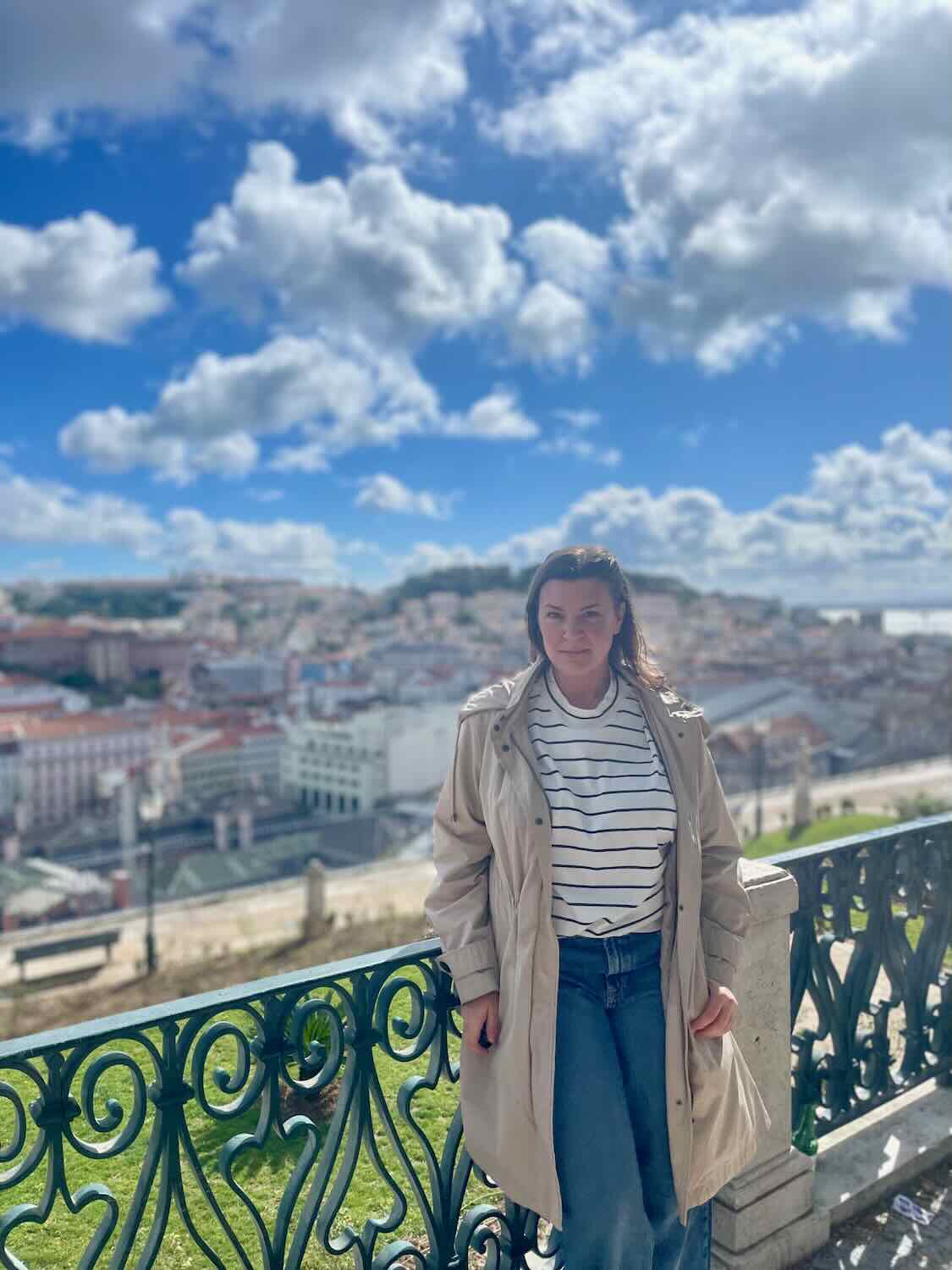 A woman traveler enjoys the view from a high vantage point in Lisbon, overlooking the city's rooftops under a partly cloudy sky