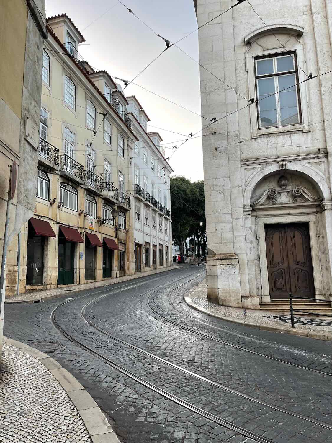A serene morning view of the empty, curving streets in Lisbon, characterized by traditional architecture and tram lines, evoking a sense of tranquility.