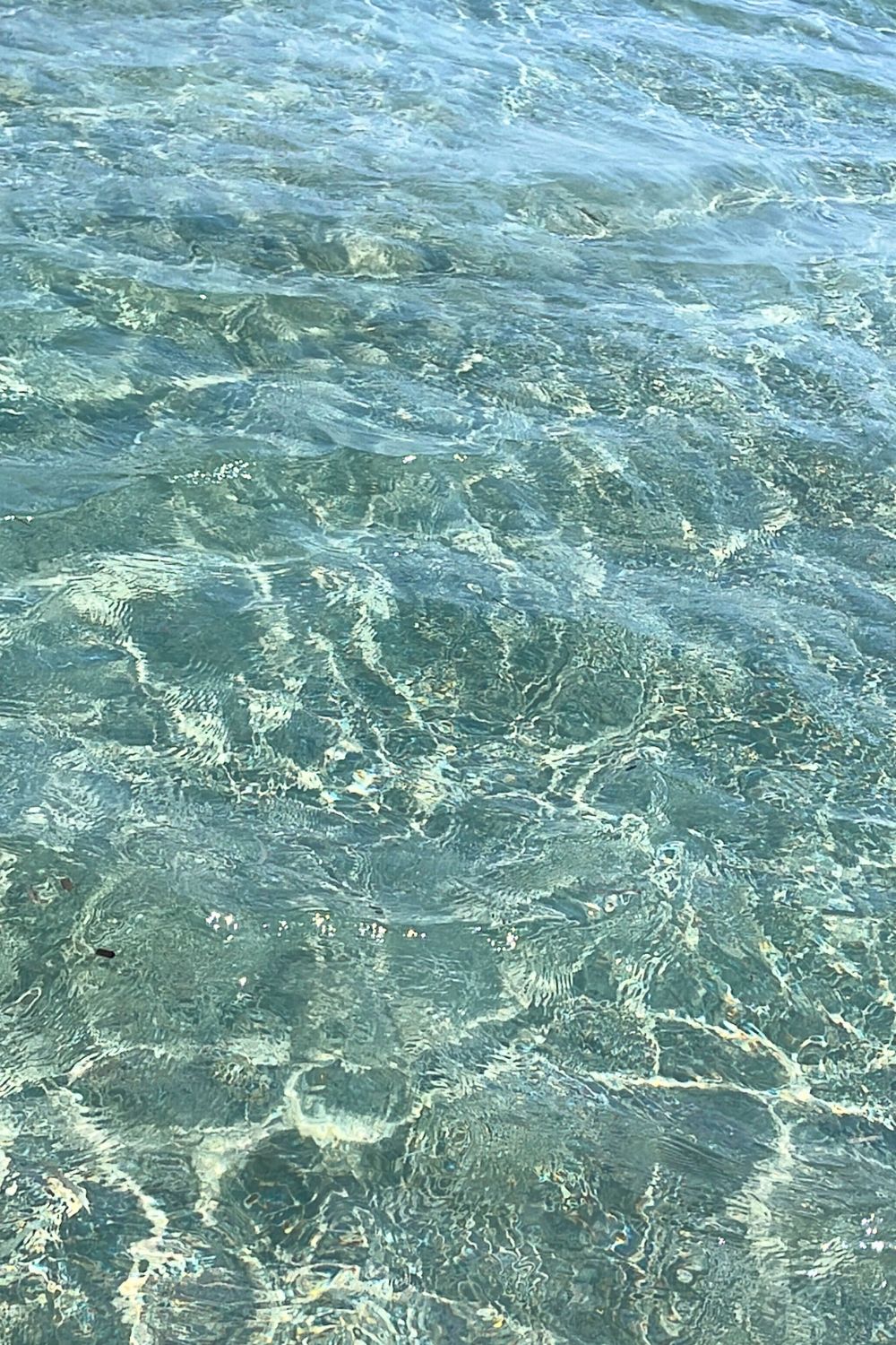 Crystal-clear waters of Faros beach in Sifnos, with visitors enjoying the calm sea and a picturesque hillside in the background.