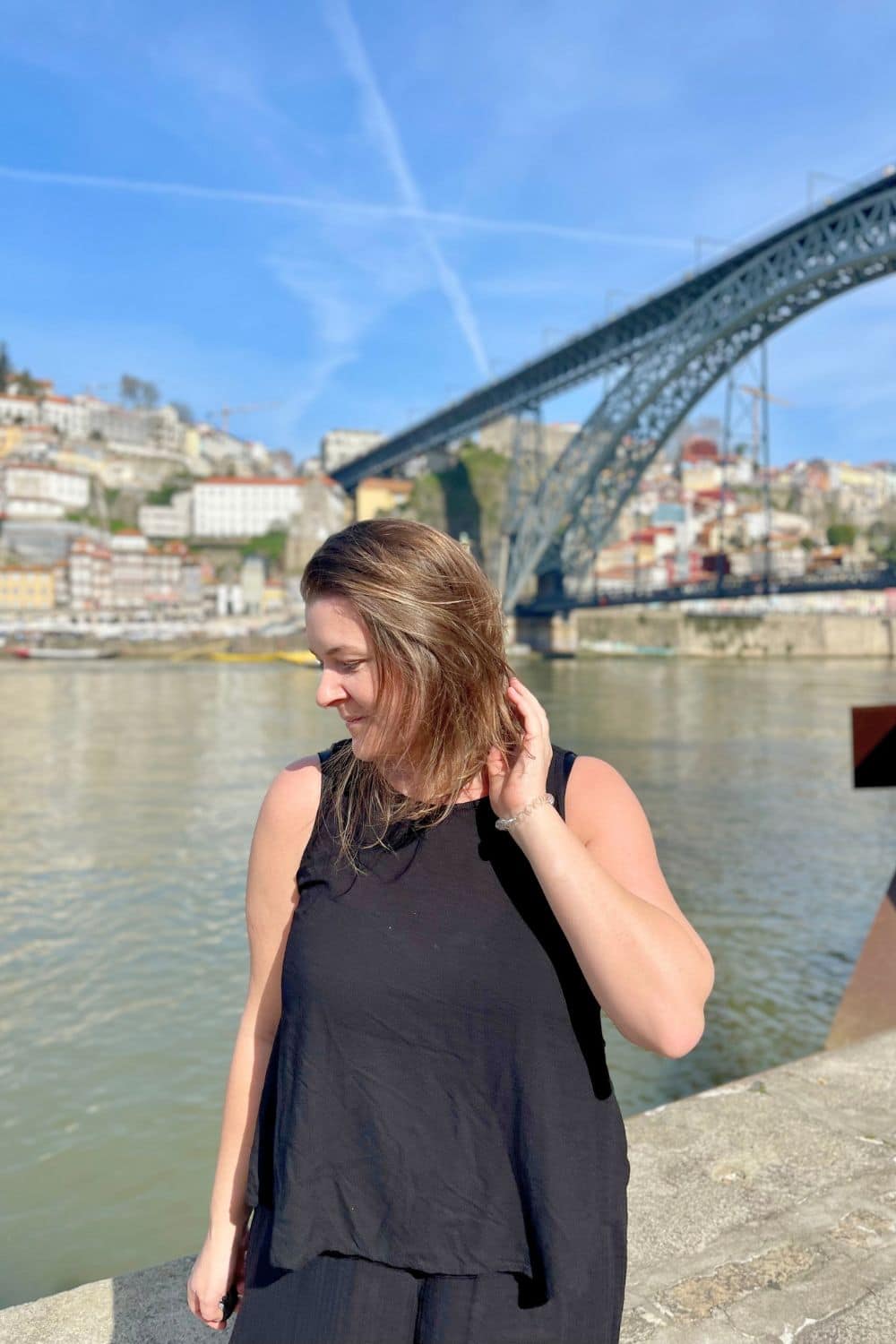 A woman standing alone in Porto with the River and bridge in the background.