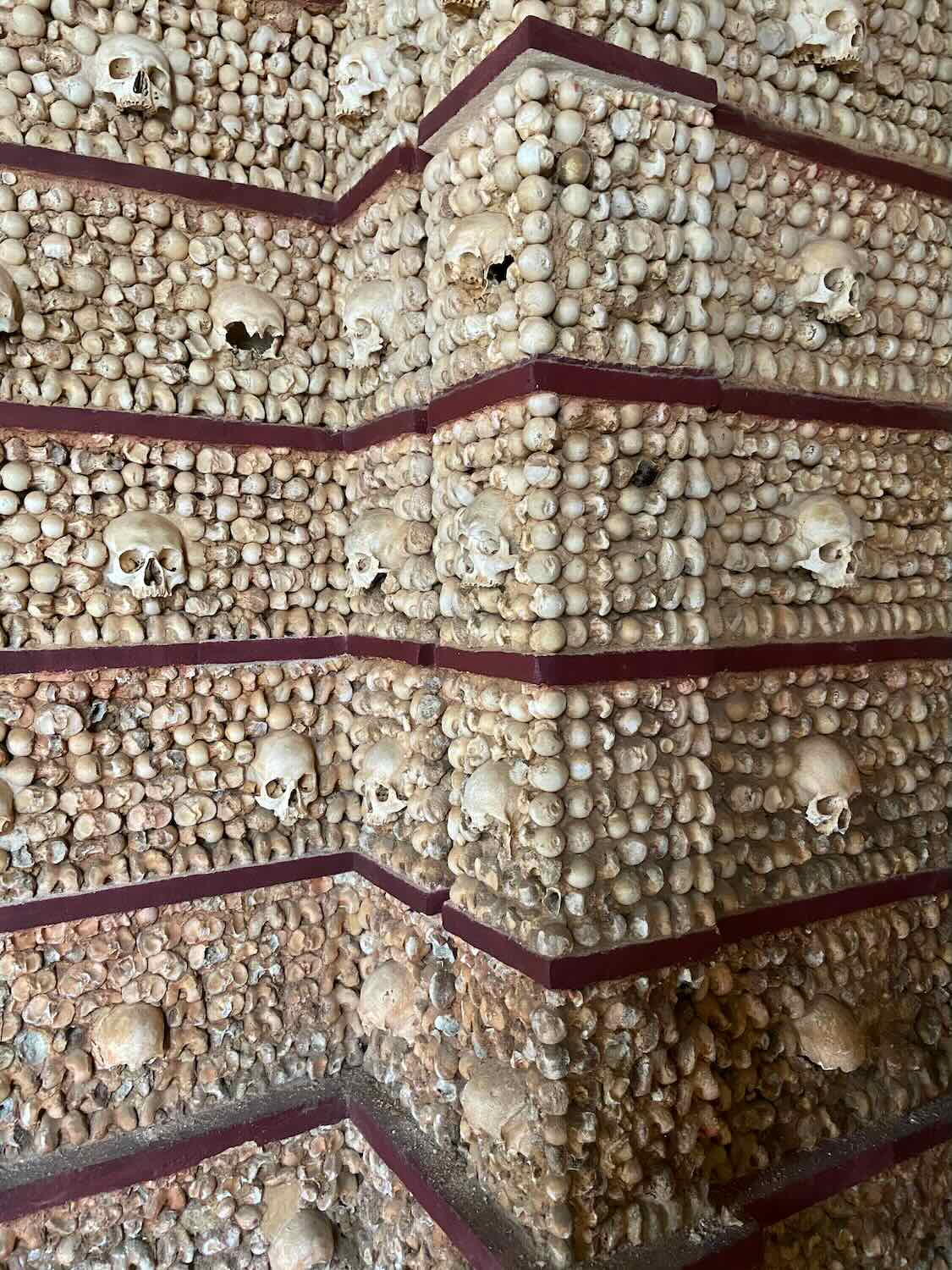 Interior detail of the Capela dos Ossos (Chapel of Bones) in Faro, walls adorned with a geometric pattern of human skulls and bones, creating a haunting yet historical atmosphere.