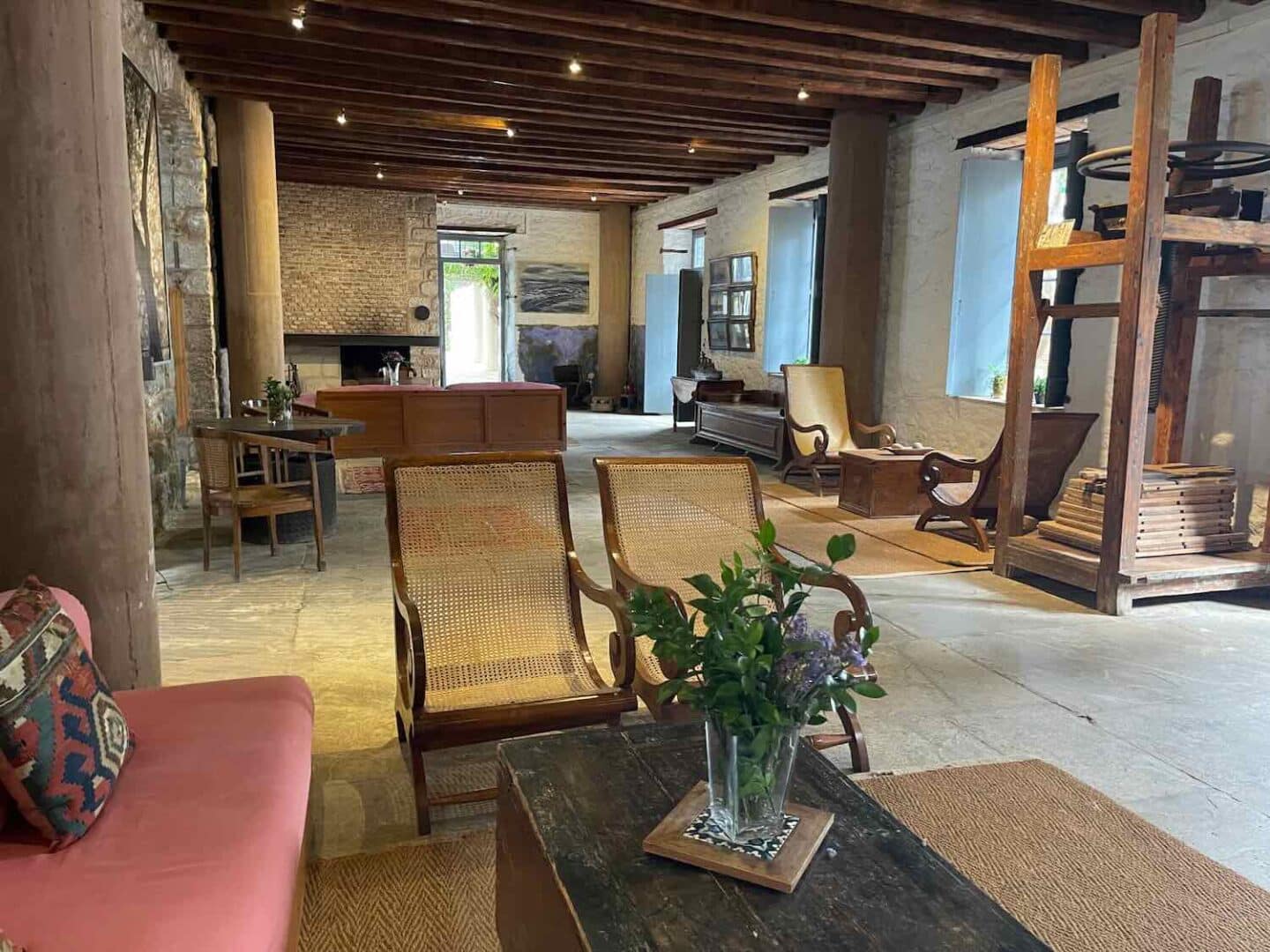 Rustic charm in a boutique hotel in Hydra, with a spacious lounge area adorned with woven chairs, a large wooden bookshelf, and a cozy fireplace.