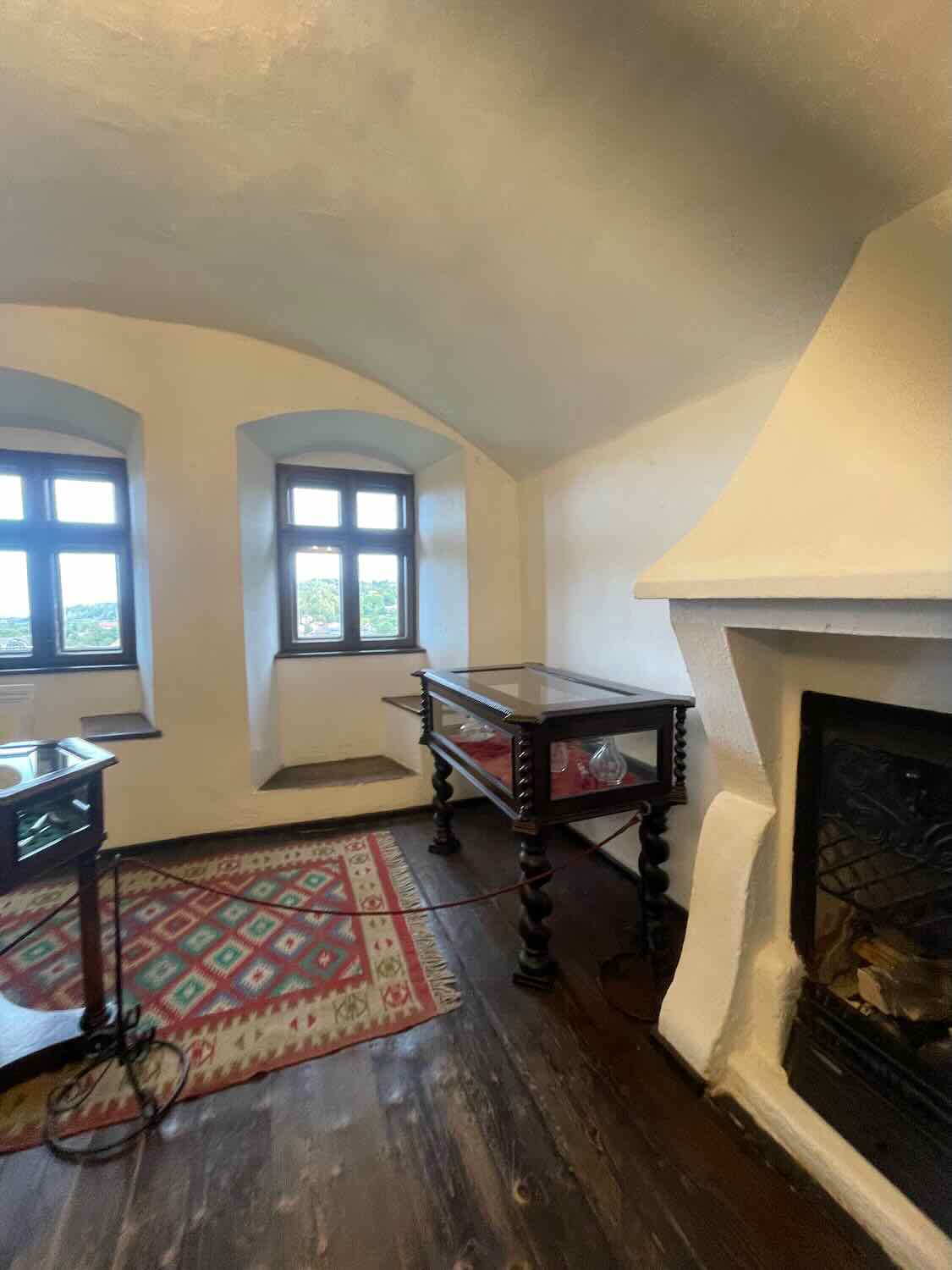 An intimate corner of a castle room featuring a traditional Romanian rug, wooden table with glass top, and a historic fireplace, invoking a sense of stepping back in time within Bran Castle.