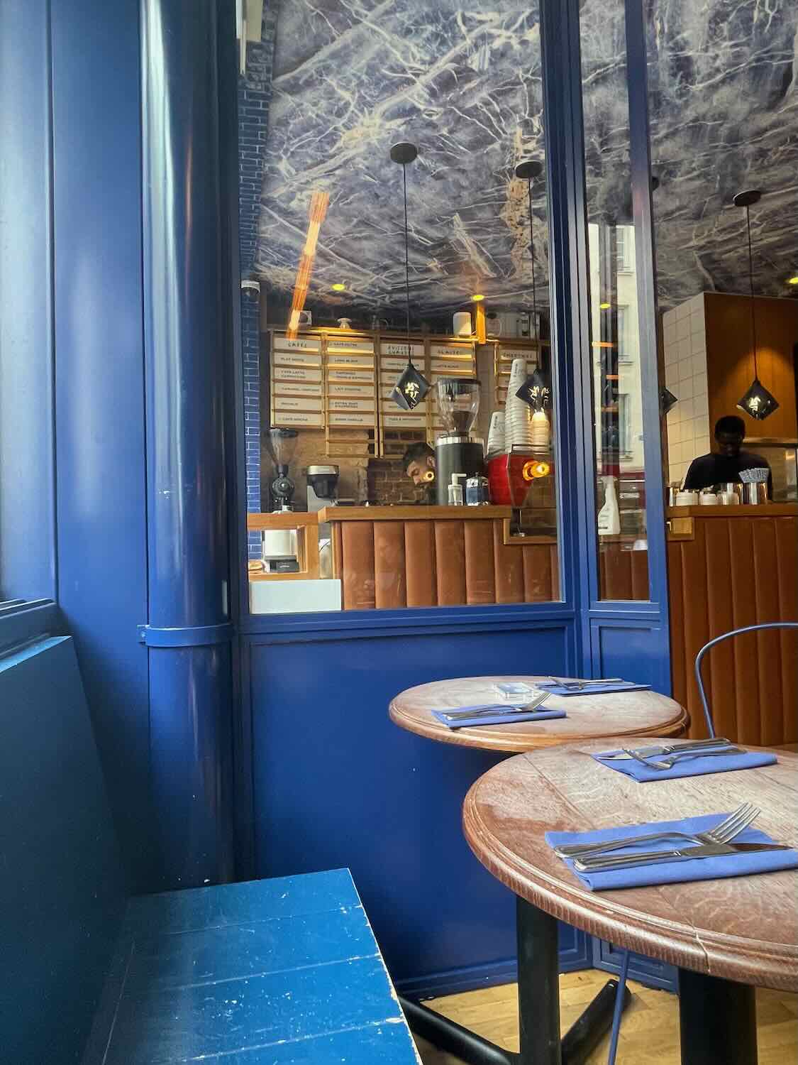 A cozy corner of a Parisian café with vibrant blue decor and wooden tables, offering a welcoming atmosphere for a leisurely coffee break.