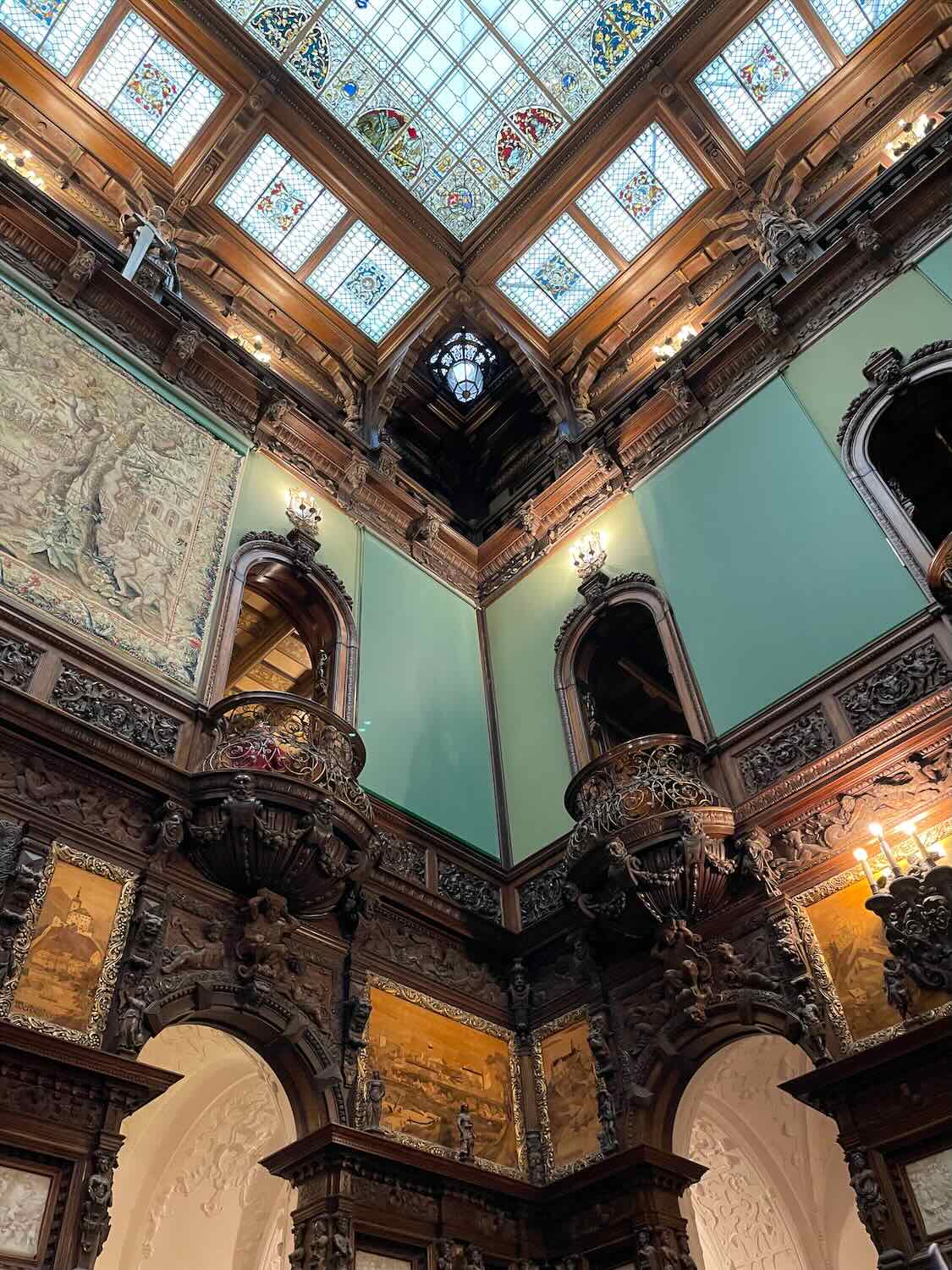 Looking up into the magnificent wooden ceiling of Peles Castle, with vibrant stained glass and intricate carvings, conveying the grandeur of Romanian royal architecture.