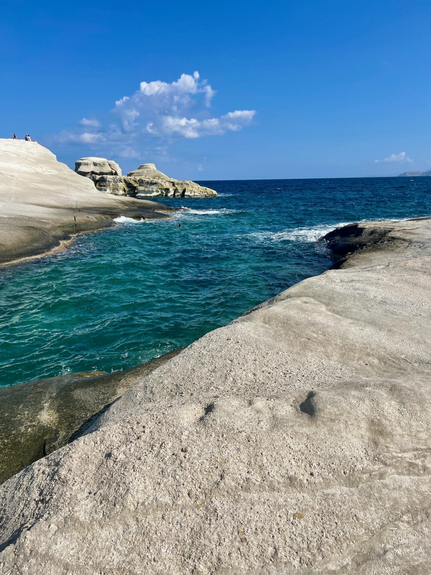 Rugged coastal landscape showcasing smooth rock formations against the deep blue waters of the sea and a partly cloudy sky.
