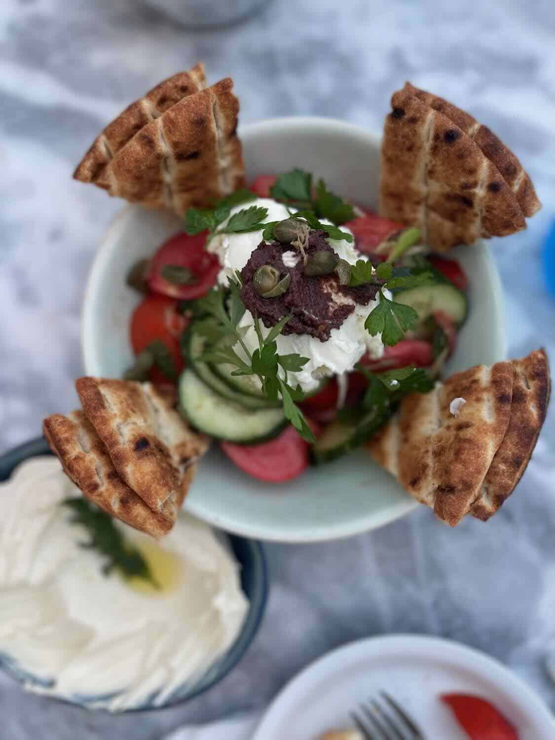 A traditional Greek salad topped with olives and feta cheese, served alongside creamy tzatziki and grilled pita bread.