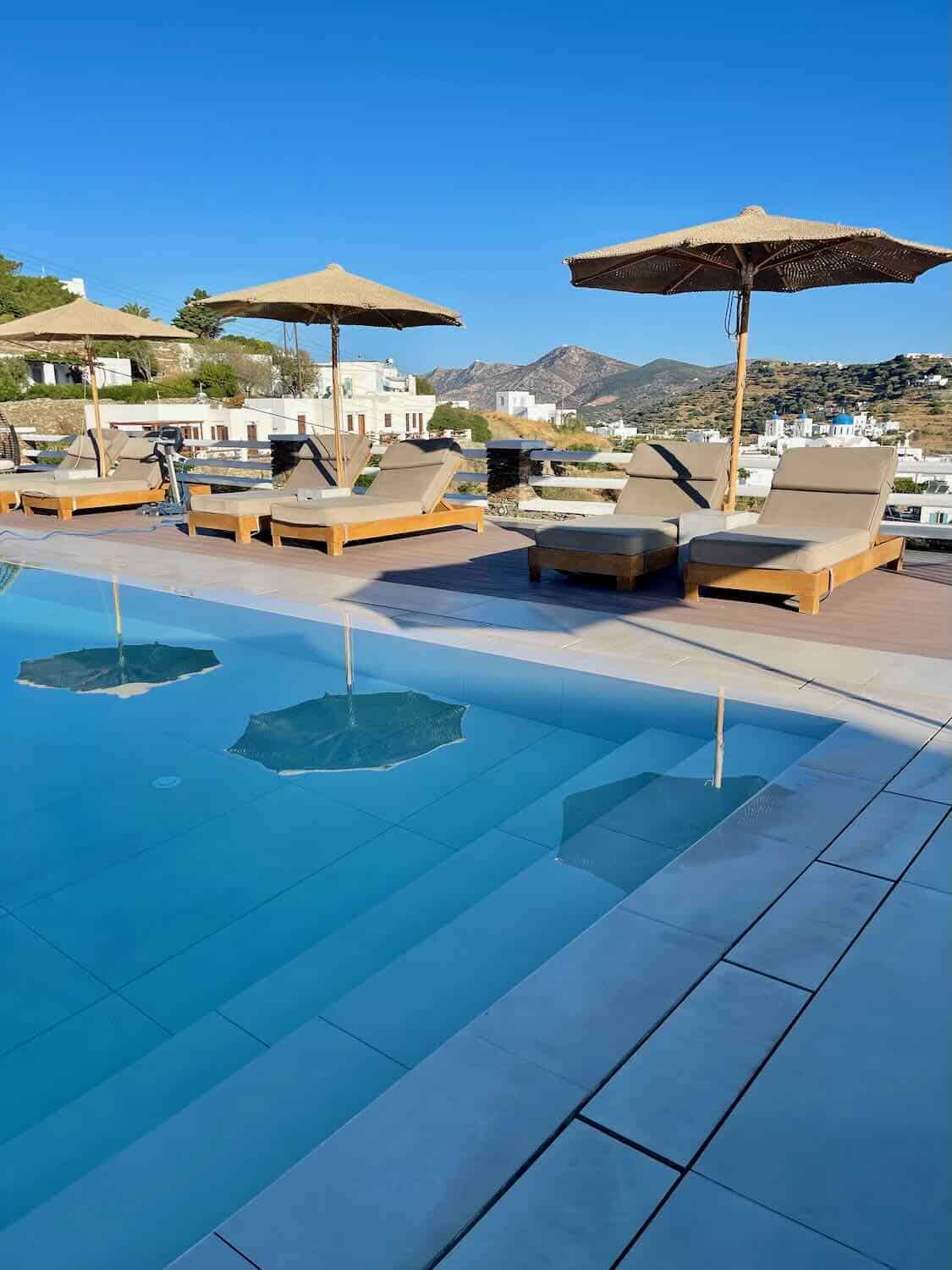 A tranquil poolside area in a Sifnos hotel, surrounded by vibrant bougainvillea and offering a panoramic view of the island,