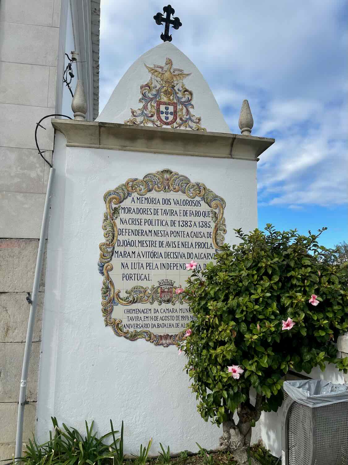 Historic plaque commemorating the valiant residents of Tavira and Faro from the political crisis of 1833-1835, adorned with the Portuguese coat of arms and flanked by pink flowers, in Tavira