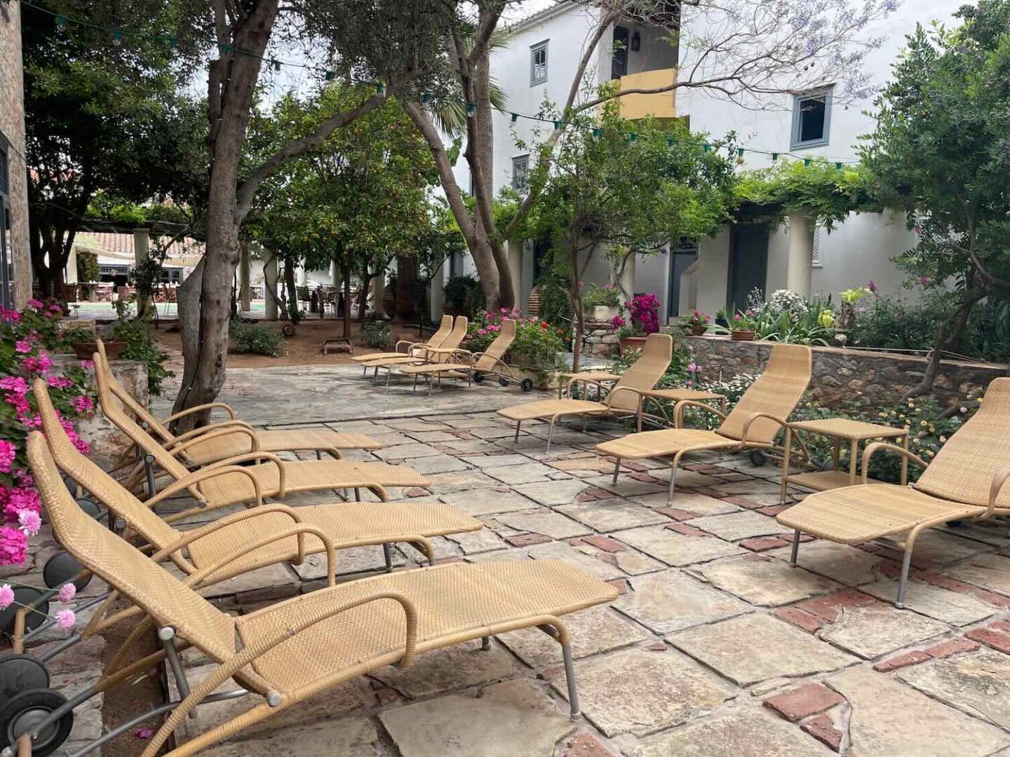 Tranquil outdoor seating area at a Hydra hotel, with wicker chairs surrounded by lush greenery and vibrant flowers, ideal for enjoying the island's peaceful ambiance.