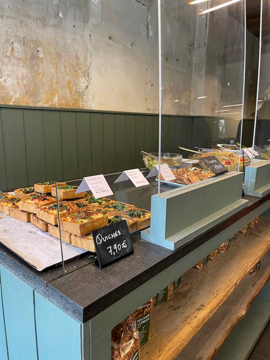 A selection of freshly baked quiches on display at a Parisian bakery, each priced at 7.90€. The counter has a rustic feel with a glass barrier and neatly labeled items.