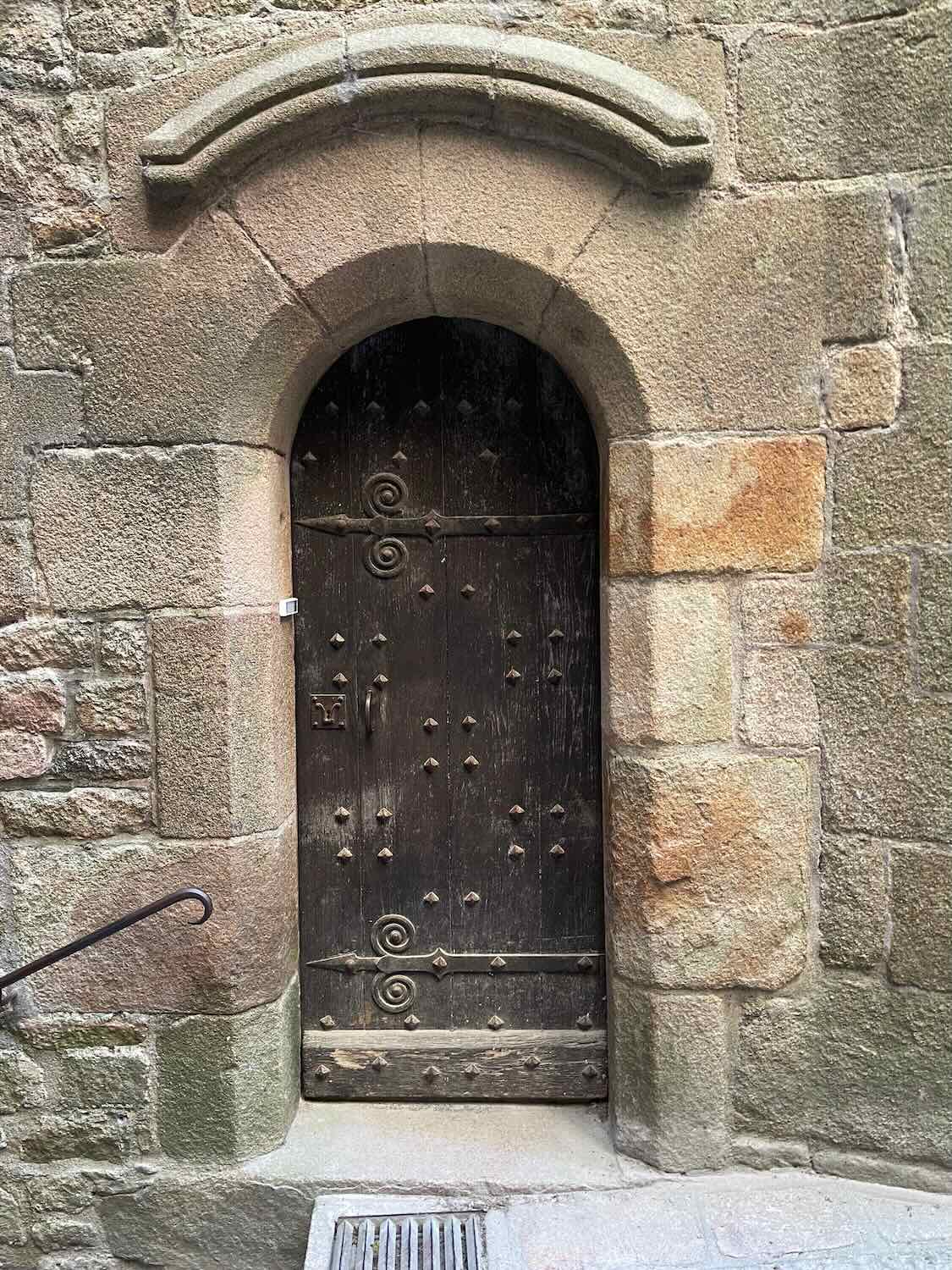 A rustic ancient wooden door set in a stone archway, featuring intricate iron details and studs, at Mont Saint-Michel.