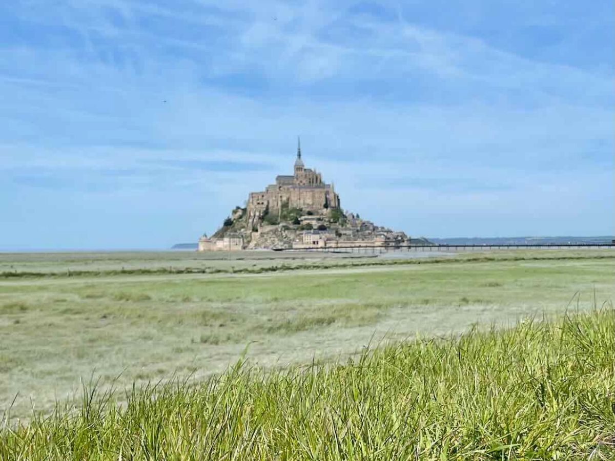 View of Mont Saint-Michel from a grassy field, showcasing the island's grandeur and unique location, posing the question of its worth as a travel destination.