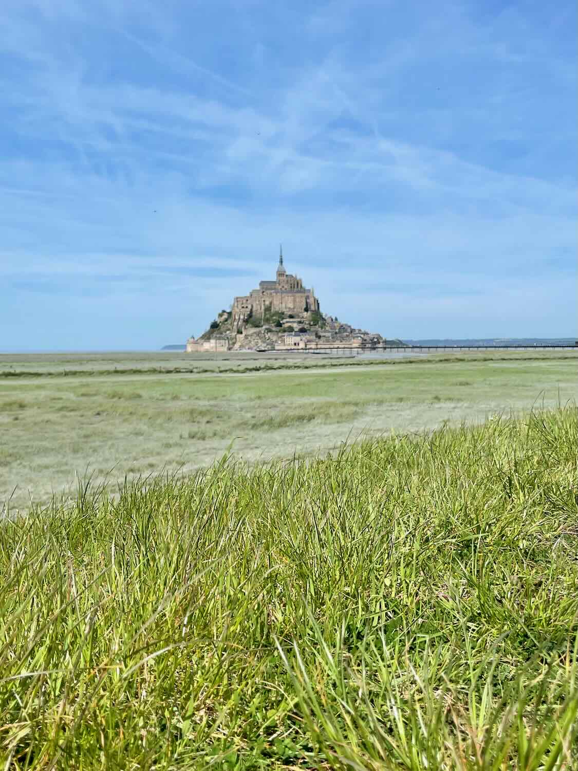 Distant view of Mont Saint Michel from a grassy field, emphasizing the vast scale and isolated position of the island.