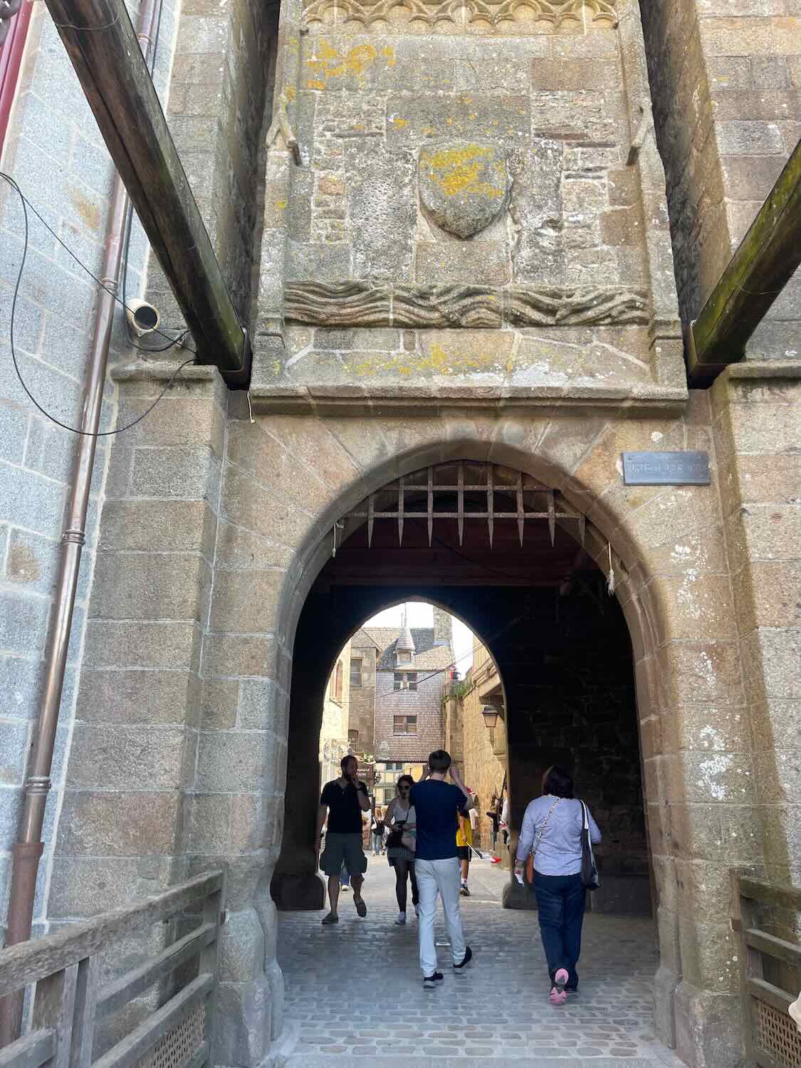Visitors walk through a medieval stone archway leading into Mont Saint Michel, highlighting the historic and preserved architecture.