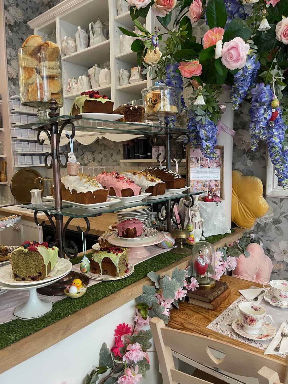 A quaint Parisian cake shop, lavishly decorated with flowers and an array of cakes displayed on elegant stands, creating a charming and inviting atmosphere.