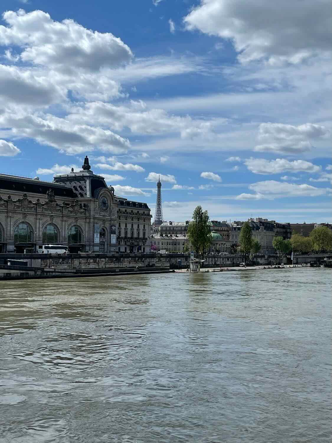 A clear day view of the Seine River with the Musée d'Orsay on one bank and the Eiffel Tower in the far background, showcasing Paris's iconic architecture and waterways.